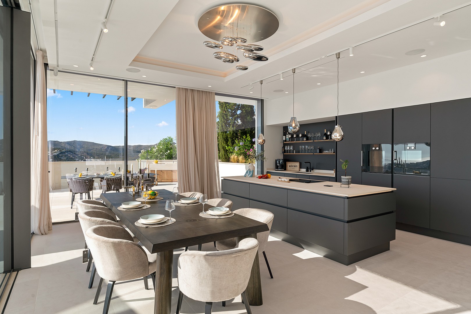 Modern open-plan kitchen and dining area with dark cabinetry, large center island, and views to an outdoor terrace.