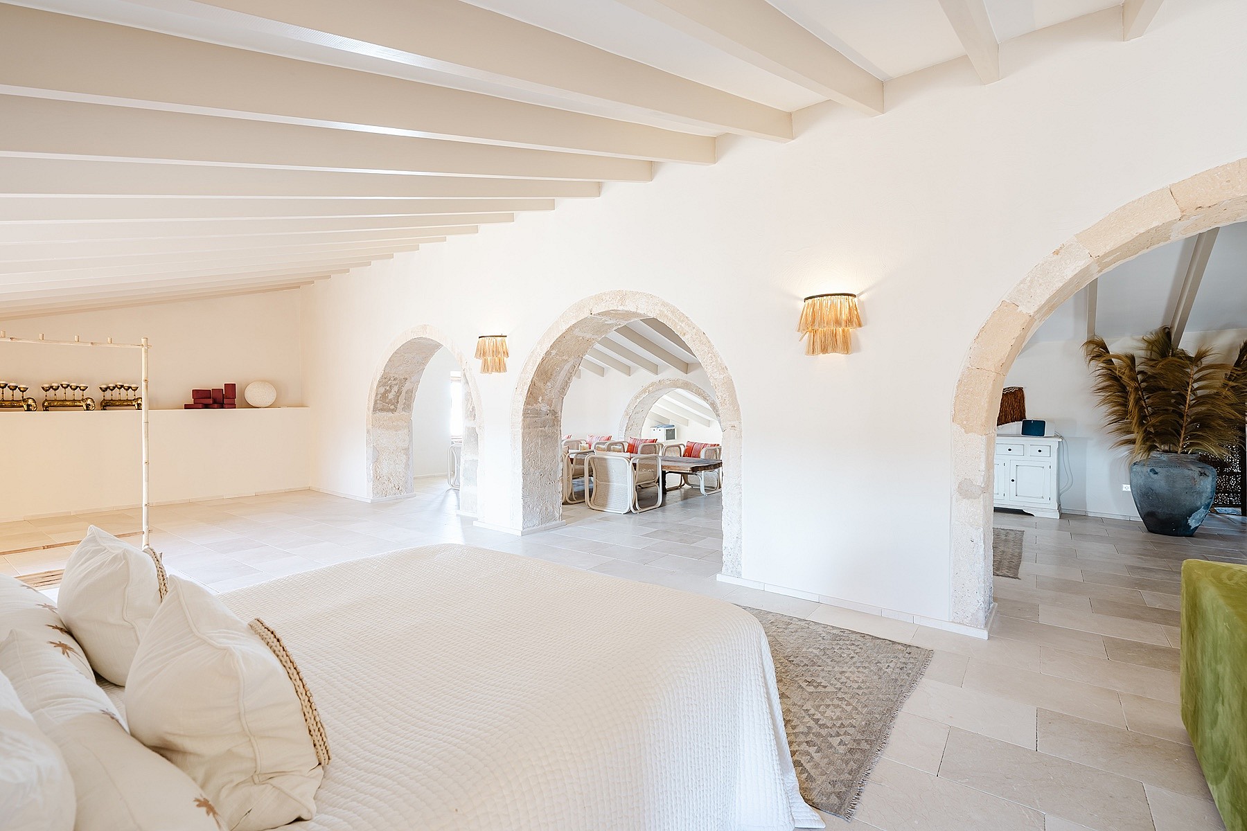 A spacious bedroom featuring white vaulted ceilings, limestone arches, and light stone flooring in a historic townhouse.