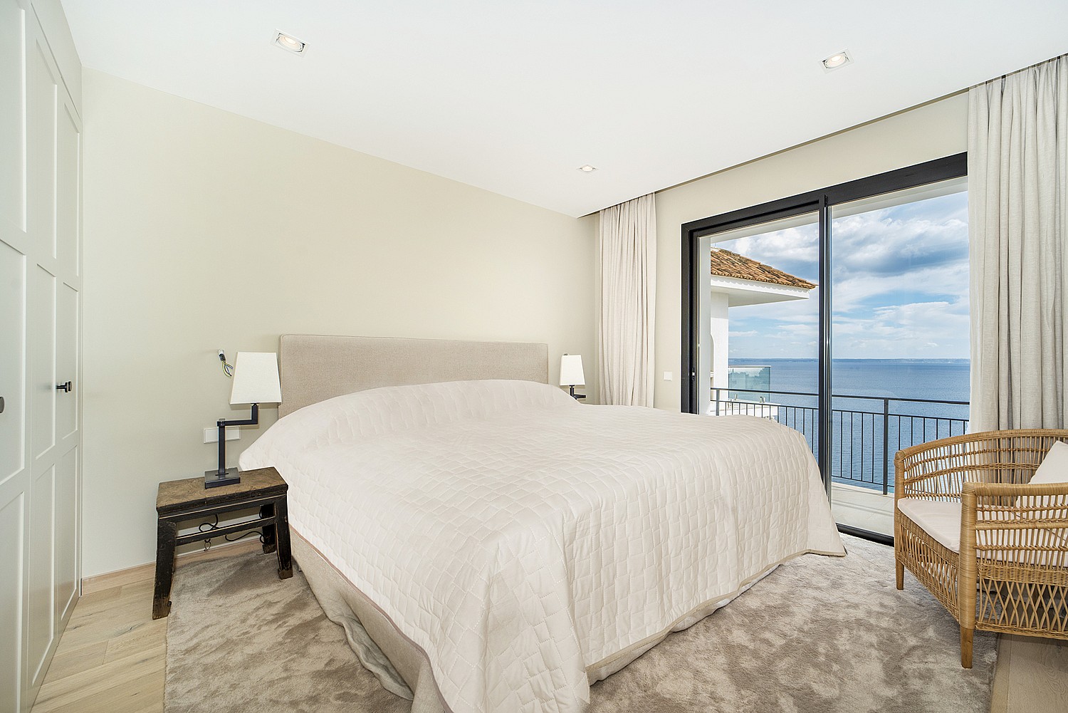 A master bedroom featuring a large bed, built-in wardrobes, and sliding glass doors opening to a terrace with ocean views.