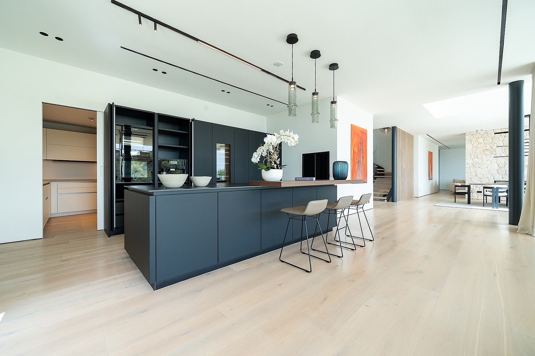 A modern kitchen with a dark grey central island, light timber flooring, and minimalist white cabinetry in a large open space.