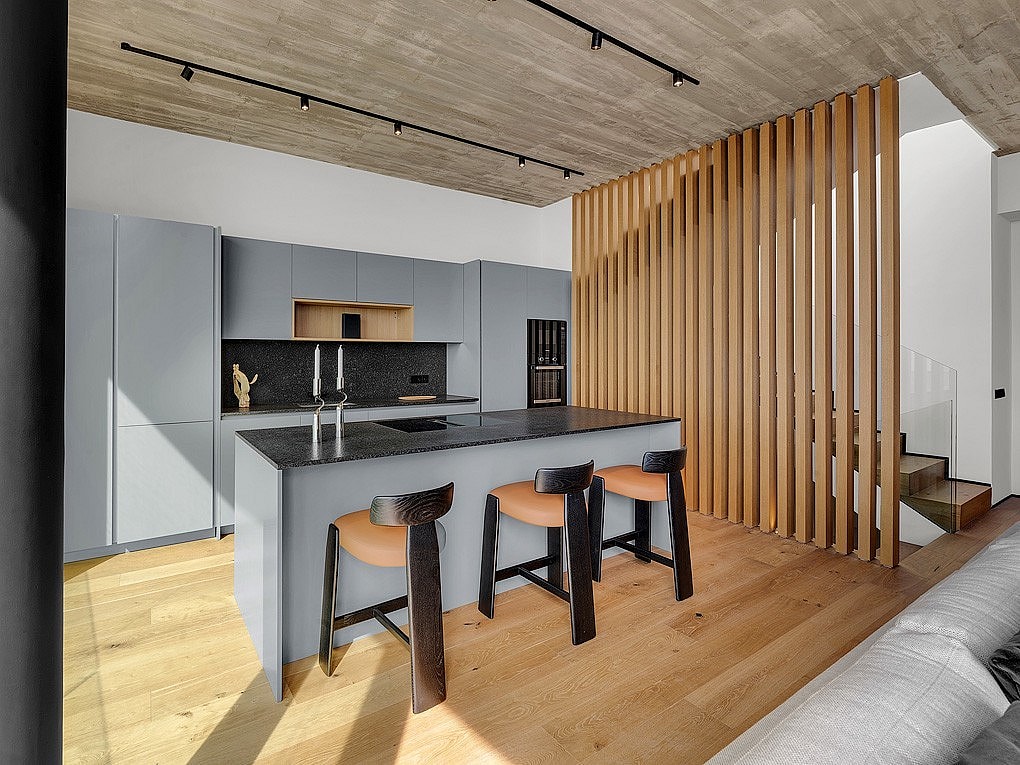 Modern open-plan kitchen featuring a gray island, oak wood slat room divider, light wood flooring, and track lighting.