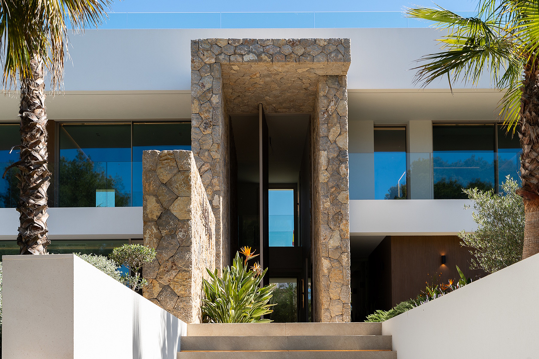 Front entrance of a modern villa featuring a central stone-clad column, white exterior walls, and a recessed doorway.