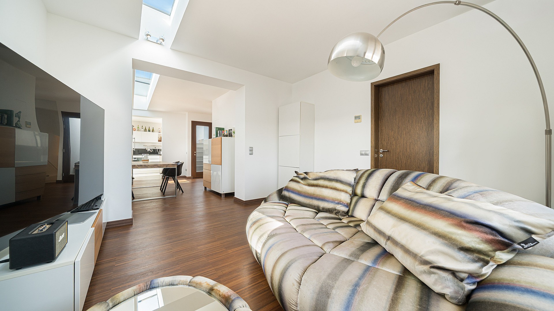 Modern living room with a large curved sofa, wooden floors, and natural light from a ceiling skylight.