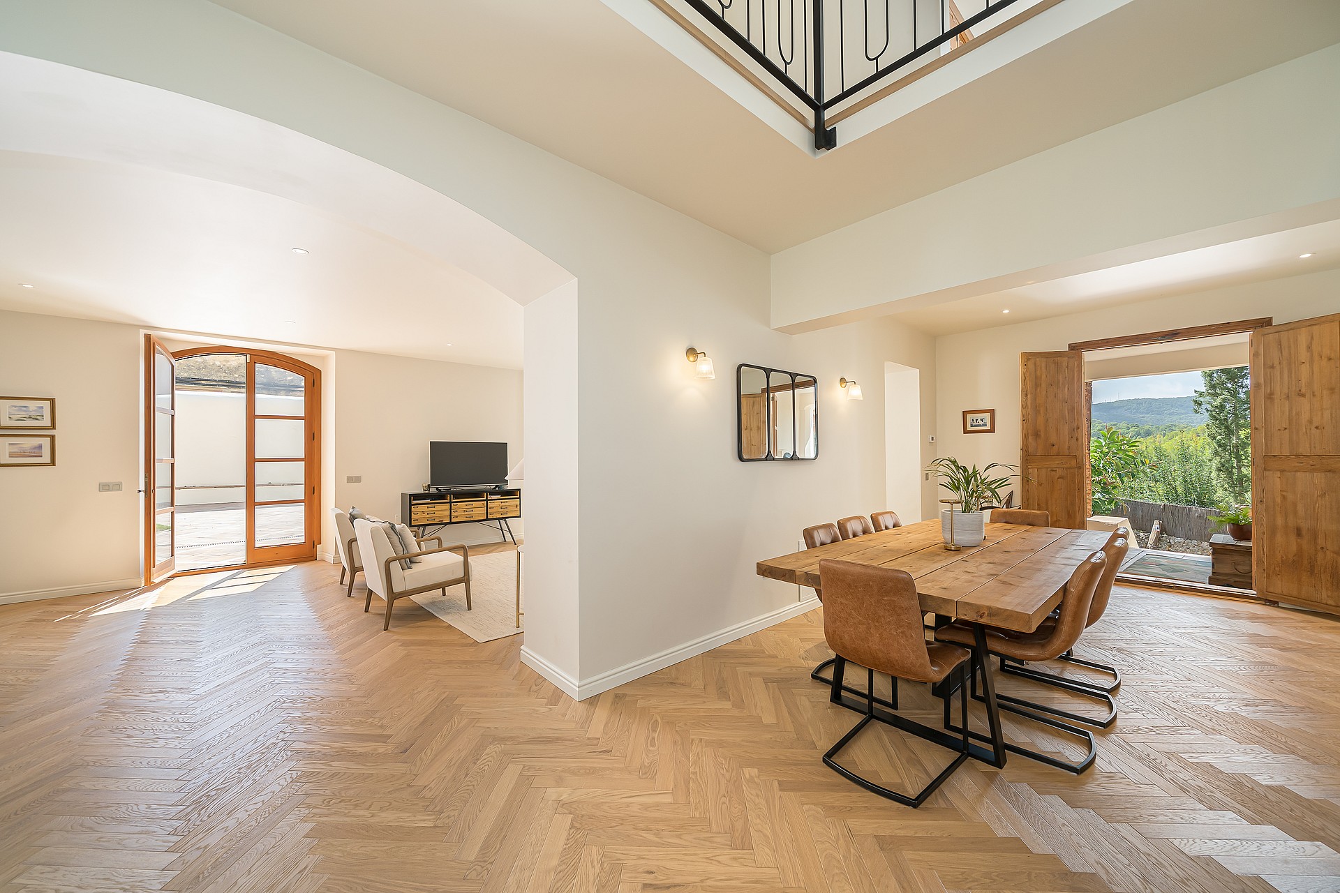 Dining room featuring a rustic wooden table, leather chairs, herringbone wood floors, and open doors leading to a garden.