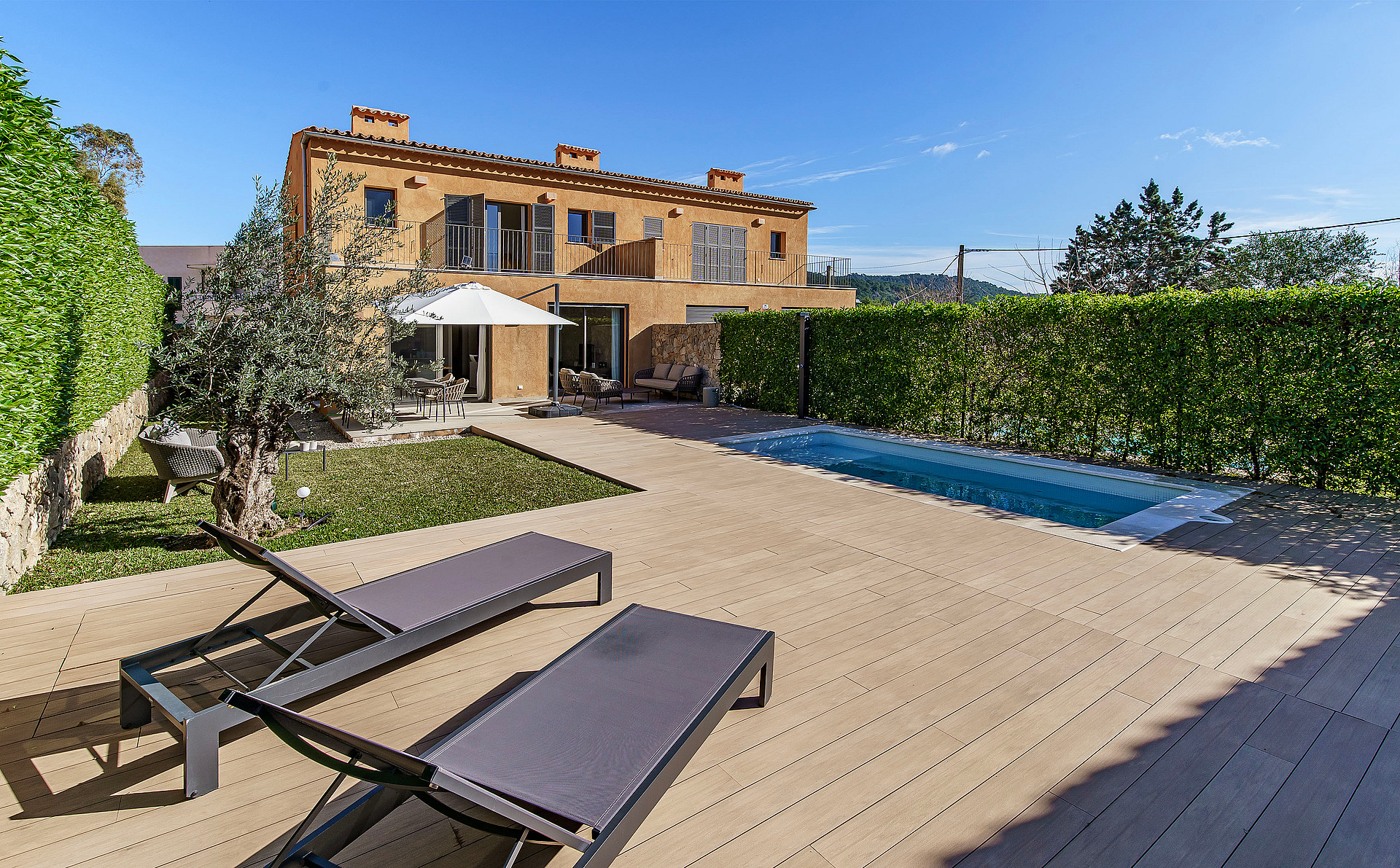 Exterior view of a Mediterranean stone townhouse with a rectangular swimming pool, sun loungers, and manicured hedge borders.