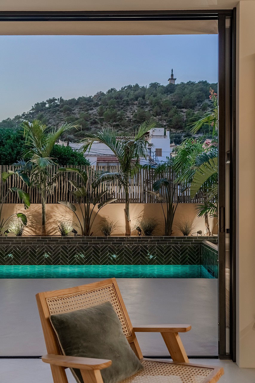 Contemporary wooden chair overlooking a dark-tiled pool and lush garden with a view of the Genova hills.