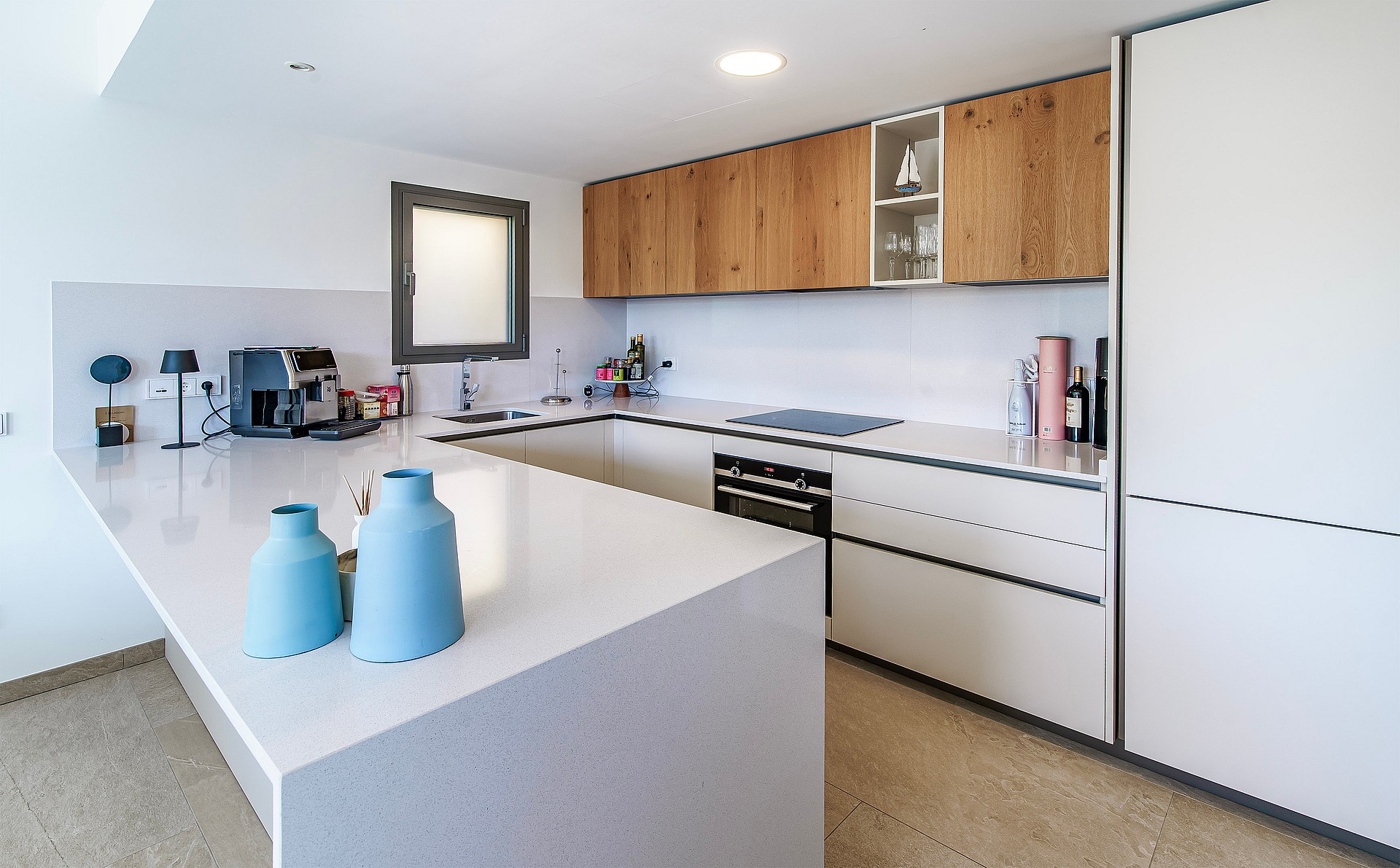 Modern U-shaped kitchen with white stone countertops, wood-veneer upper cabinets, and integrated appliances.
