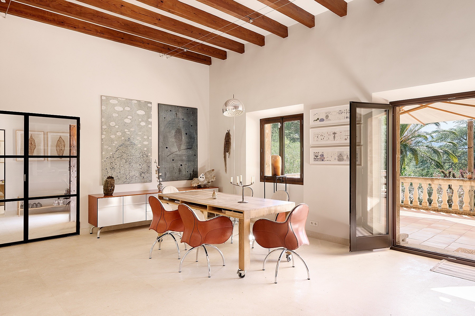 Dining room in a Finca featuring a long wooden table, leather swivel chairs, exposed ceiling beams, and a terrace doorway.