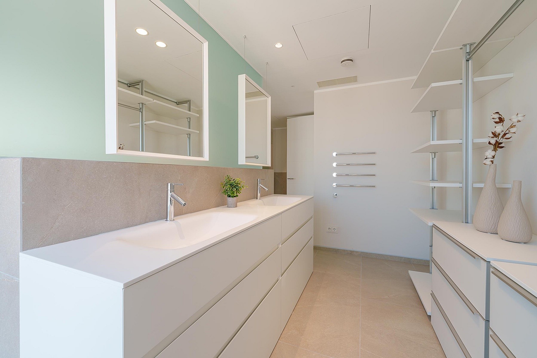 Baño moderno con doble lavabo blanco, pared verde salvia, dos espejos rectangulares y estanterías integradas.