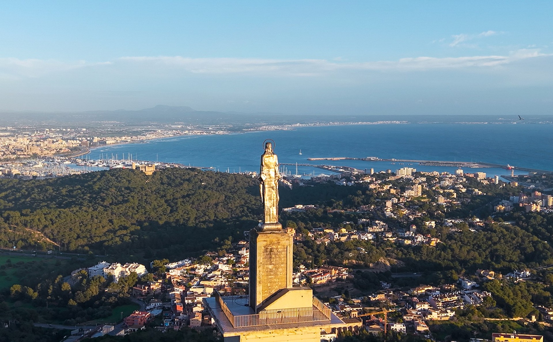 Aerial view overlooking the statue at Castell de Bellver with the city of Palma, harbor, and Mediterranean Sea in the distance.