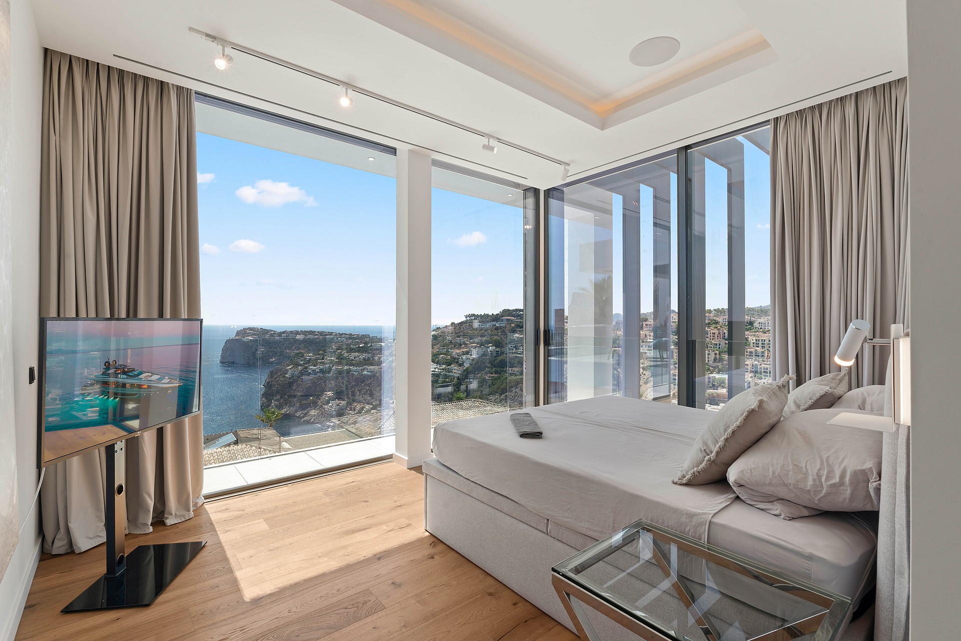 Modern bedroom featuring a king bed facing floor-to-ceiling windows overlooking a coastal cliff and sea, with light oak floors.
