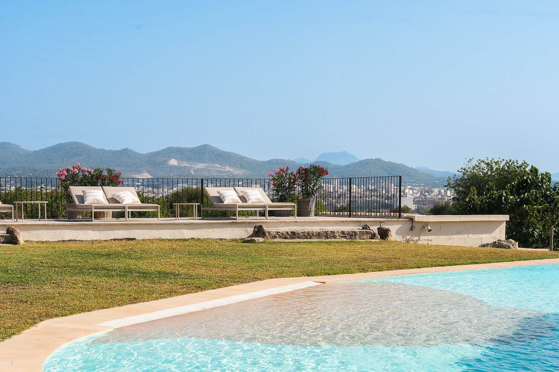Piscina exterior en primer plano con terraza de piedra y tumbonas frente a las sierras a lo lejos.