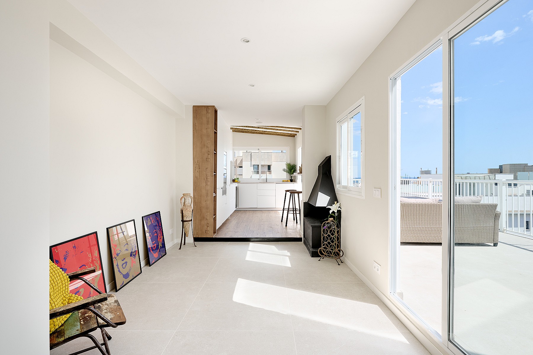 Bright living area with white walls, tile floors, and a corner fireplace, leading to an outdoor terrace with sea views.