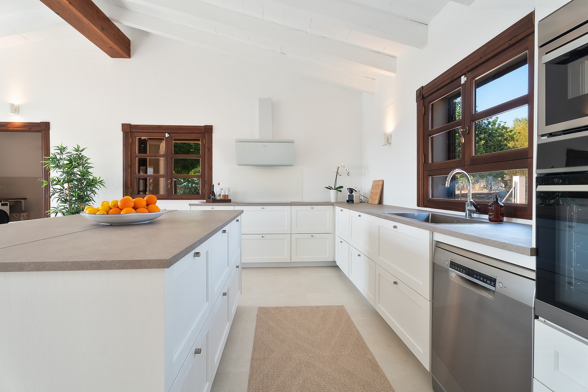 Cocina con muebles blancos, encimeras de piedra y marcos de madera bajo techos abovedados de madera blanca.