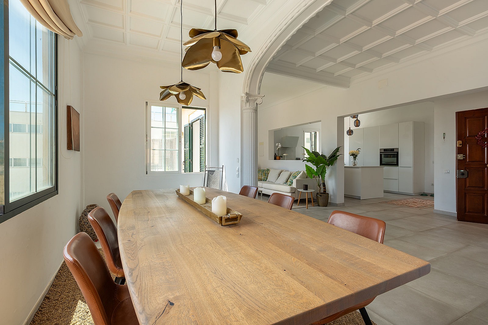 Dining area featuring a large live-edge wooden table, leather chairs, and two decorative pendant lights under a coffered ceiling.