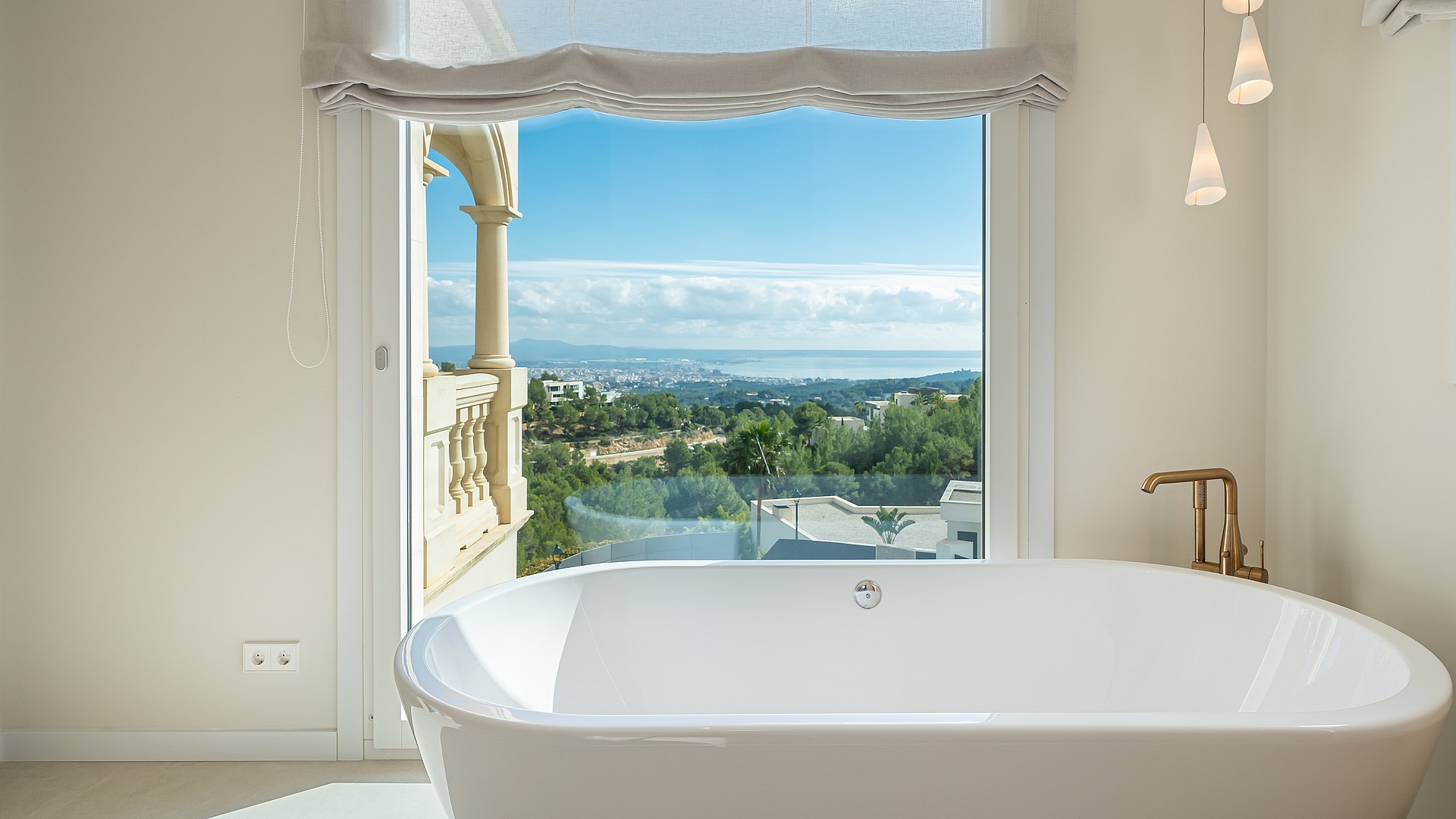 A white freestanding bathtub positioned in front of a large window with views of the coastline and Mediterranean Sea.