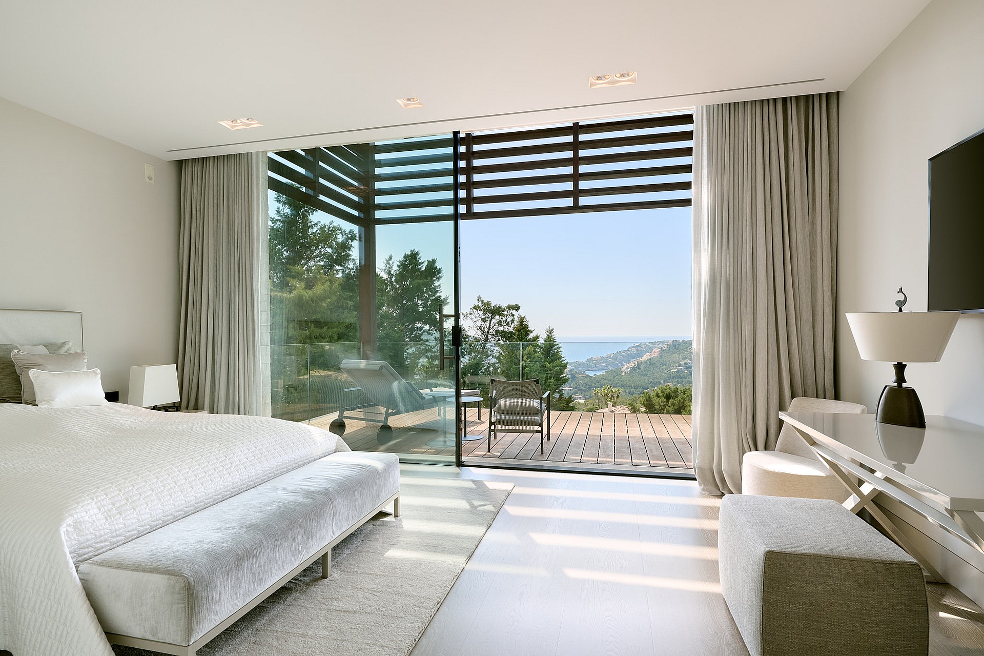 Bedroom with floor-to-ceiling glazing opening to a terrace over the sea and harbour