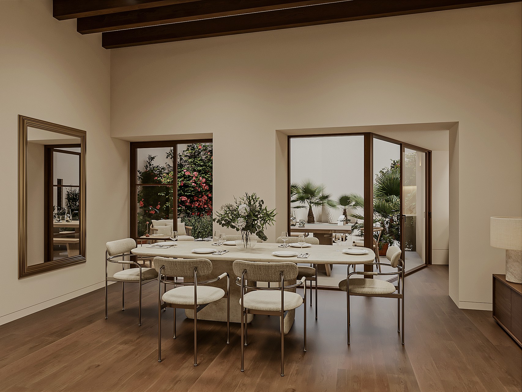 Dining table with eight chairs beside large windows and glazed doors overlooking a planted garden with bougainvillea and palms.