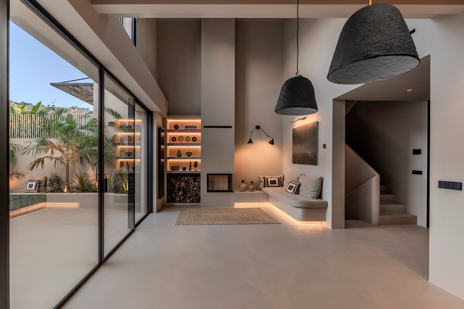 Minimalist living room featuring a tall fireplace, woven pendant lights, and large glass doors opening to a private patio.