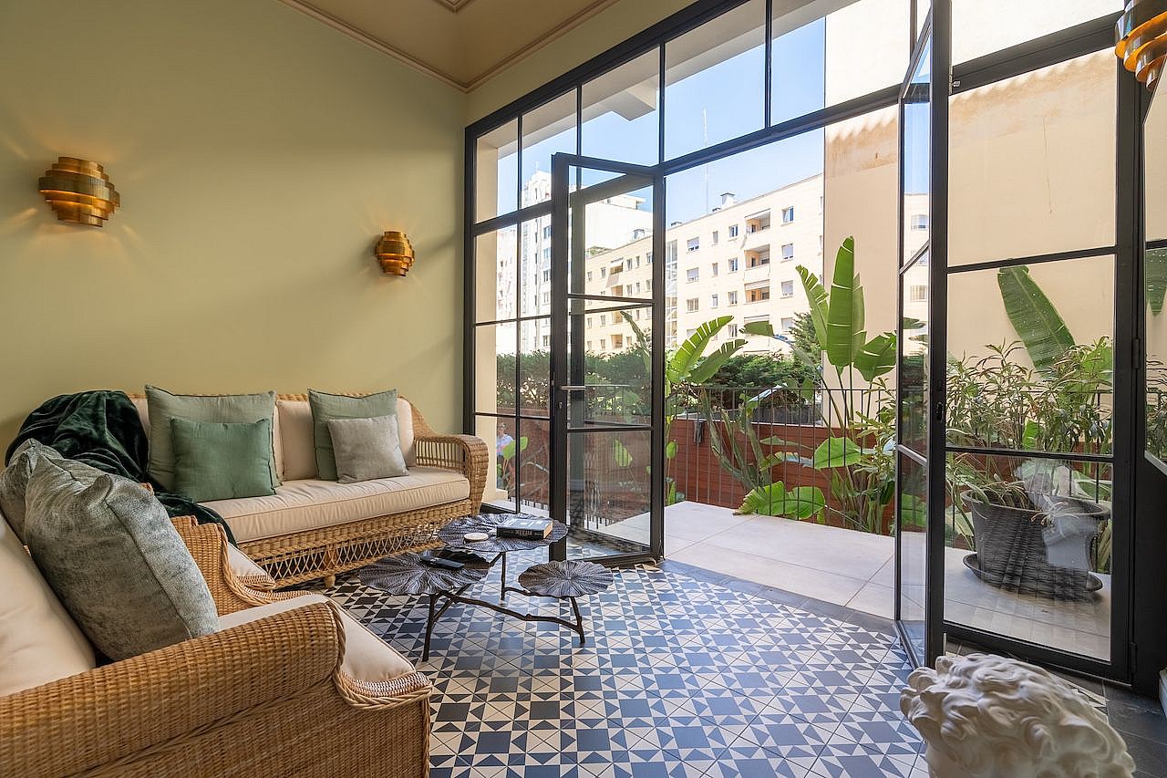 Sunroom featuring a wicker sofa, patterned ceramic floor tiles, and black-framed glass doors opening to a private patio.