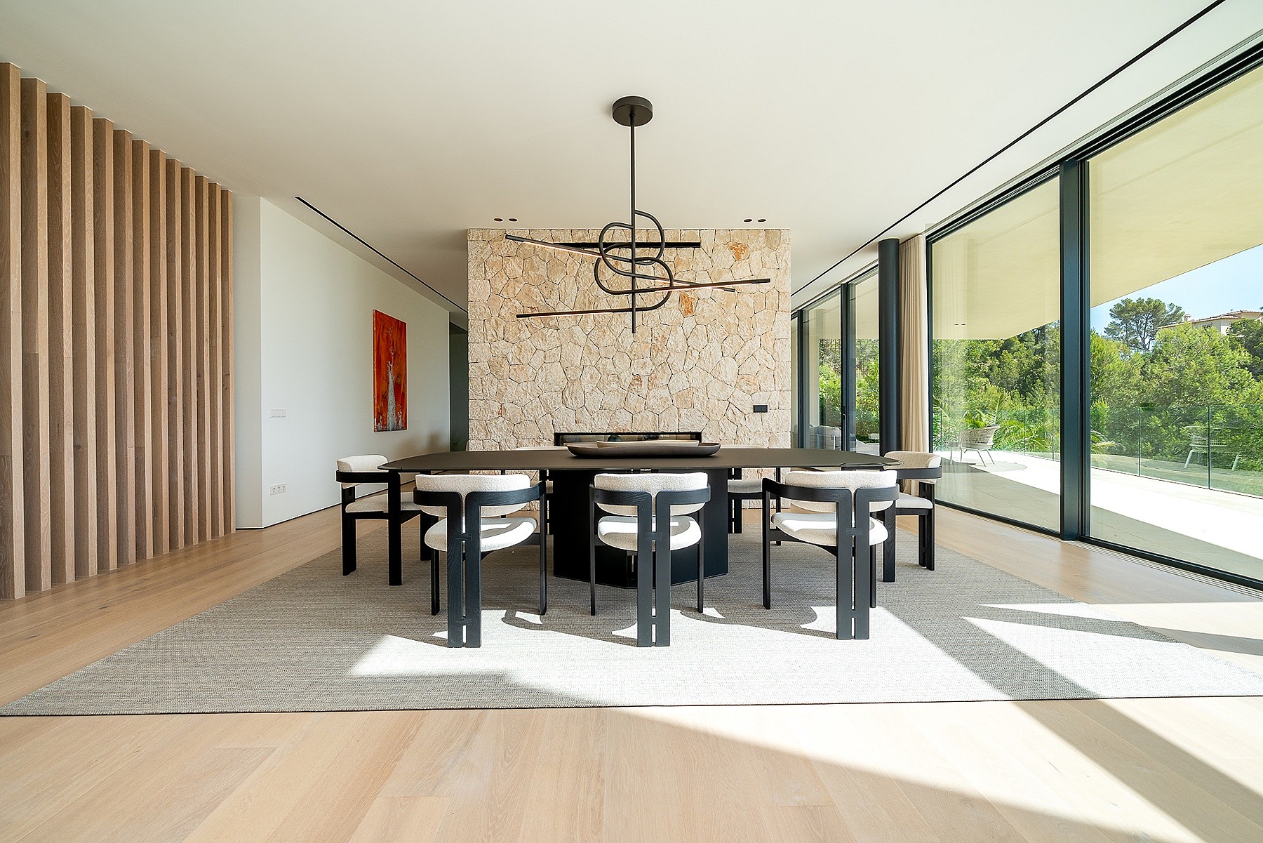 Dining area with dark rectangular table, six modern chairs, linear pendant light, and a prominent textured natural stone accent wall.