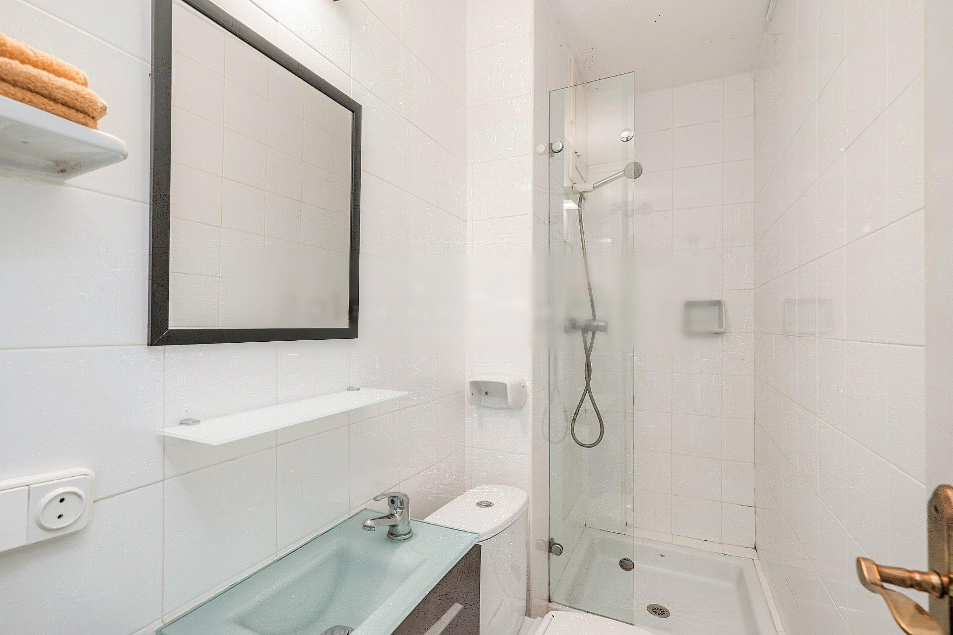 Modern bathroom with white tiled walls, a glass walk-in shower, a square mirror with a dark frame, and a glass vanity sink.