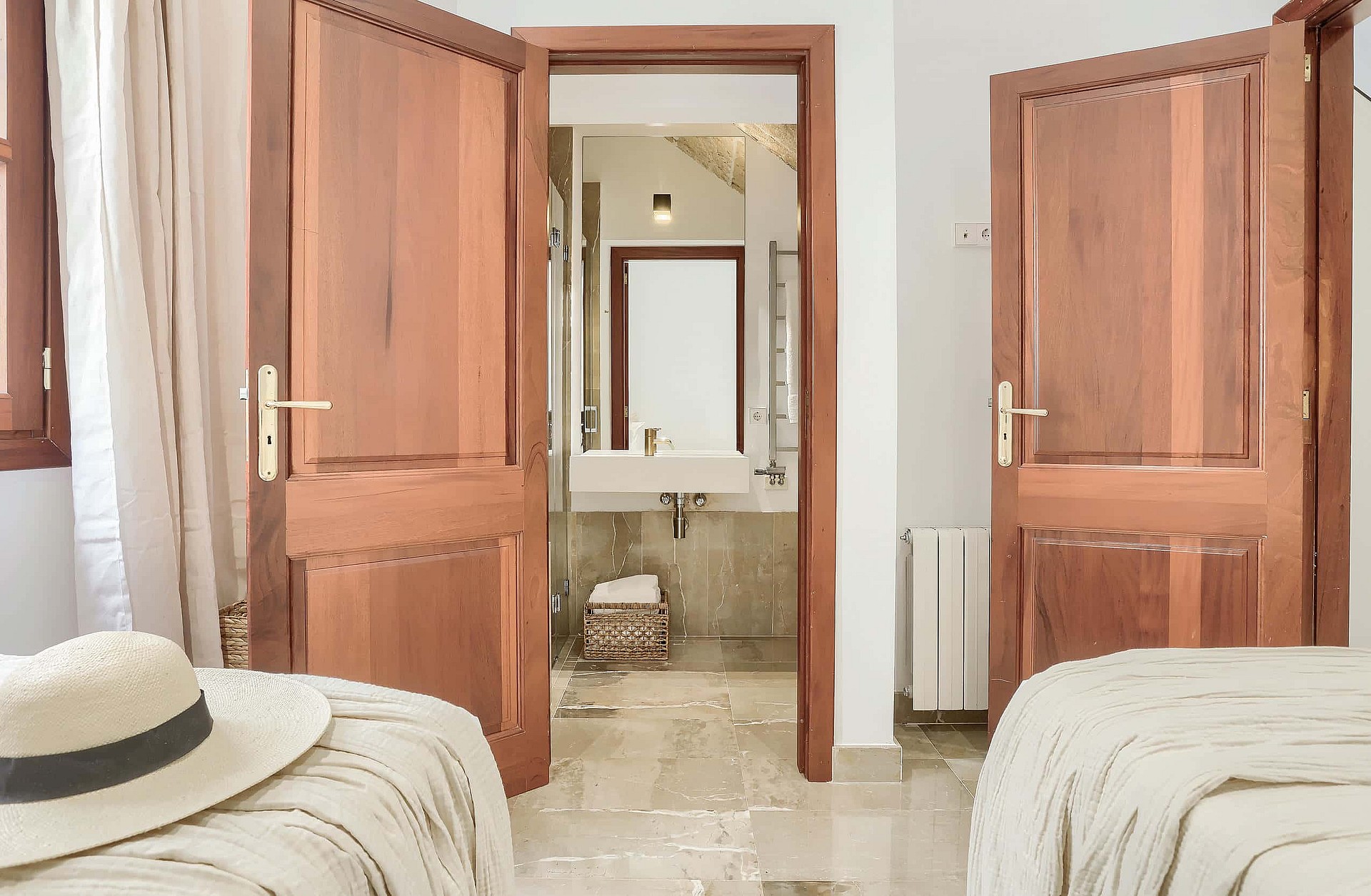 Interior view showing a bedroom leading into an en-suite bathroom through wooden double doors, featuring cream tile floors.
