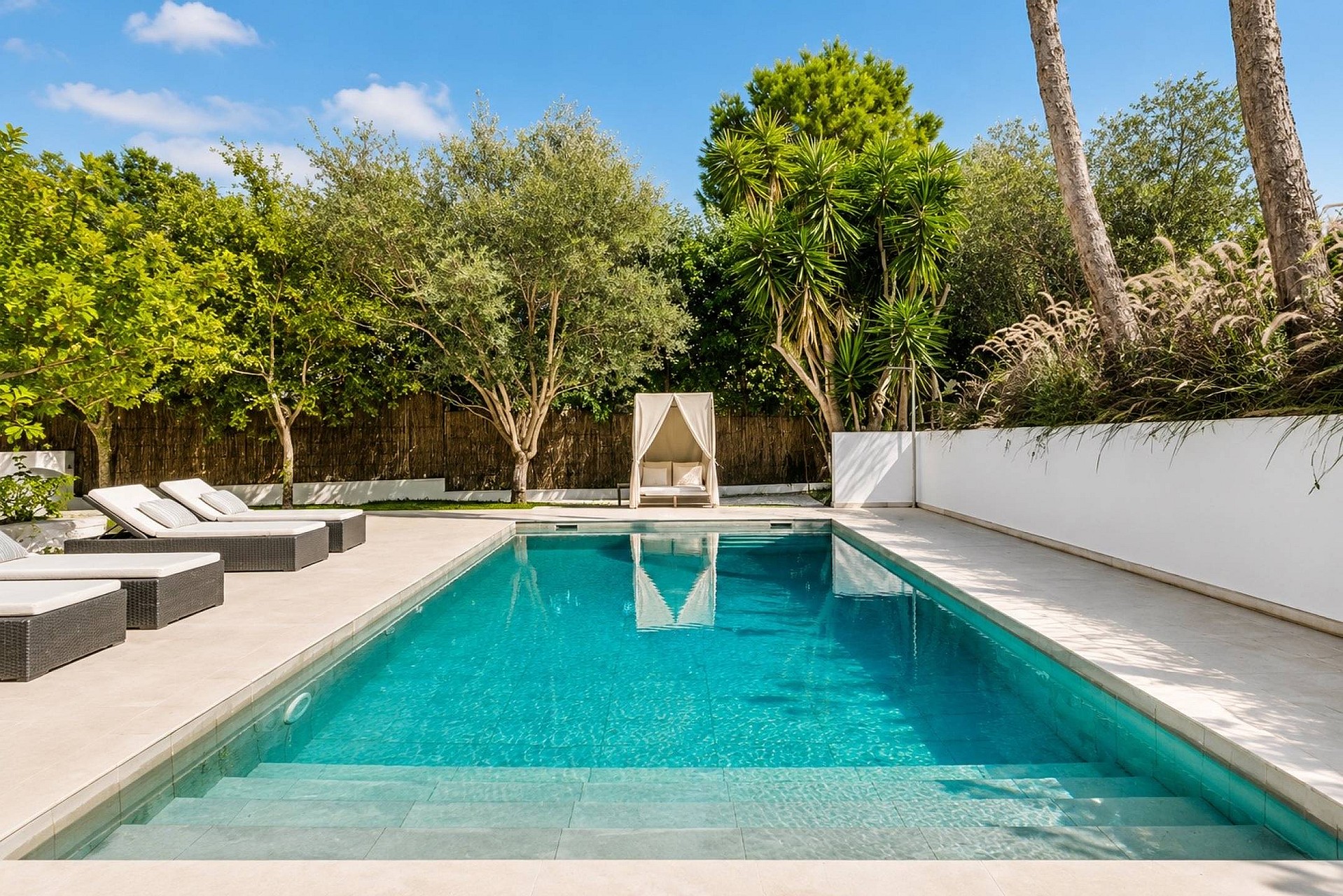 Rectangular swimming pool with tiled interior, sun loungers and canopy daybed surrounded by mature Mediterranean planting