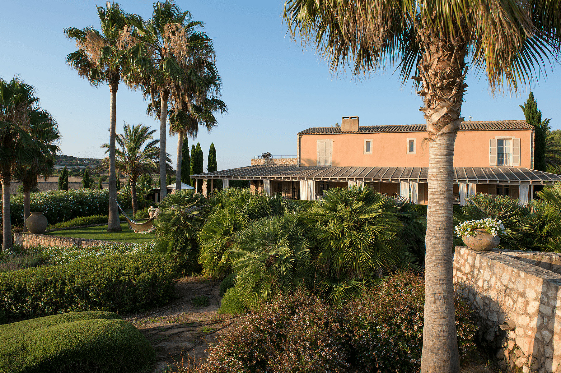 Exterior view of a terracotta-toned traditional finca building surrounded by tall palm trees and a dense Mediterranean garden.