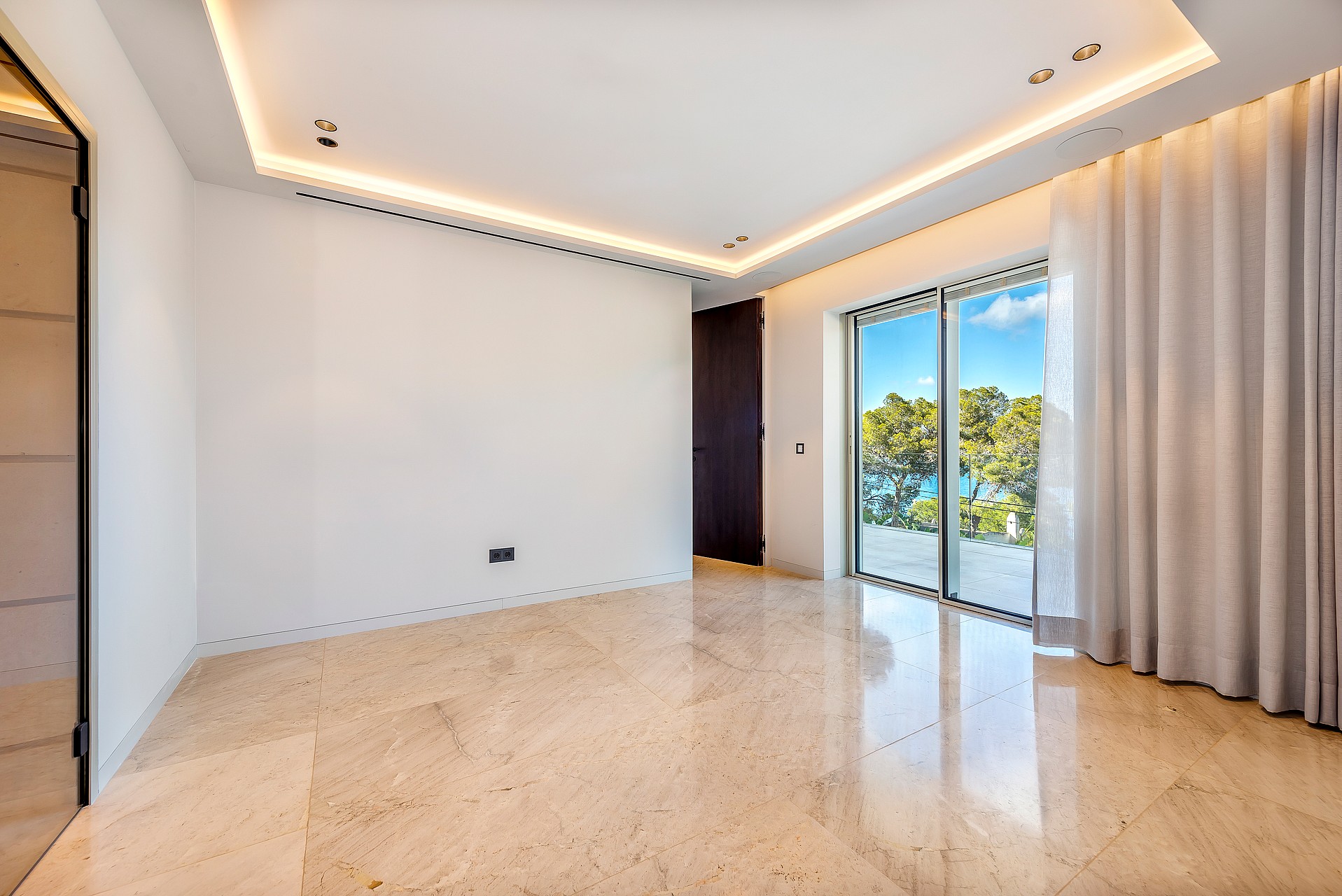 Empty modern bedroom with polished light marble floor, recessed ceiling lighting, and sliding glass doors to a balcony.