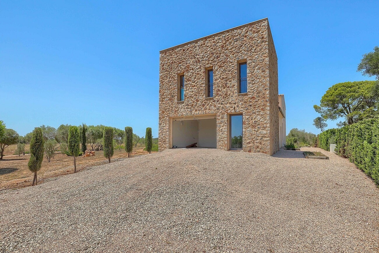 Two-story stone-clad outbuilding with narrow windows and an open ground-level portico, set against a gravel driveway.