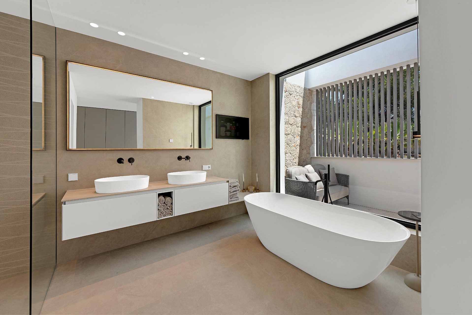 Spa-style bathroom with freestanding white bath, double vessel sinks, stone wall cladding and glazed opening to private terrace