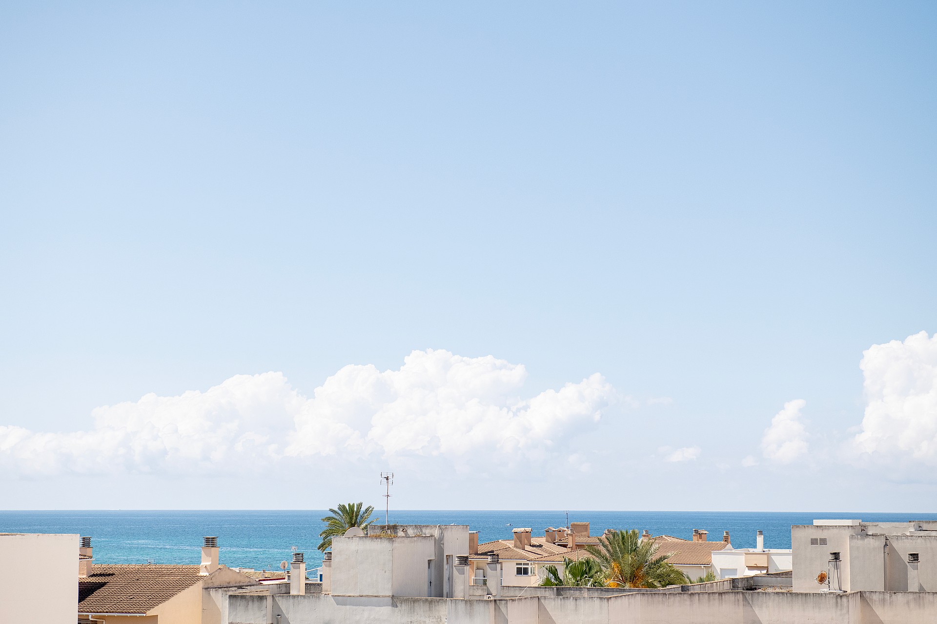 An elevated view looking out over the flat rooftops of El Molinar towards the blue Mediterranean Sea under a clear sky.