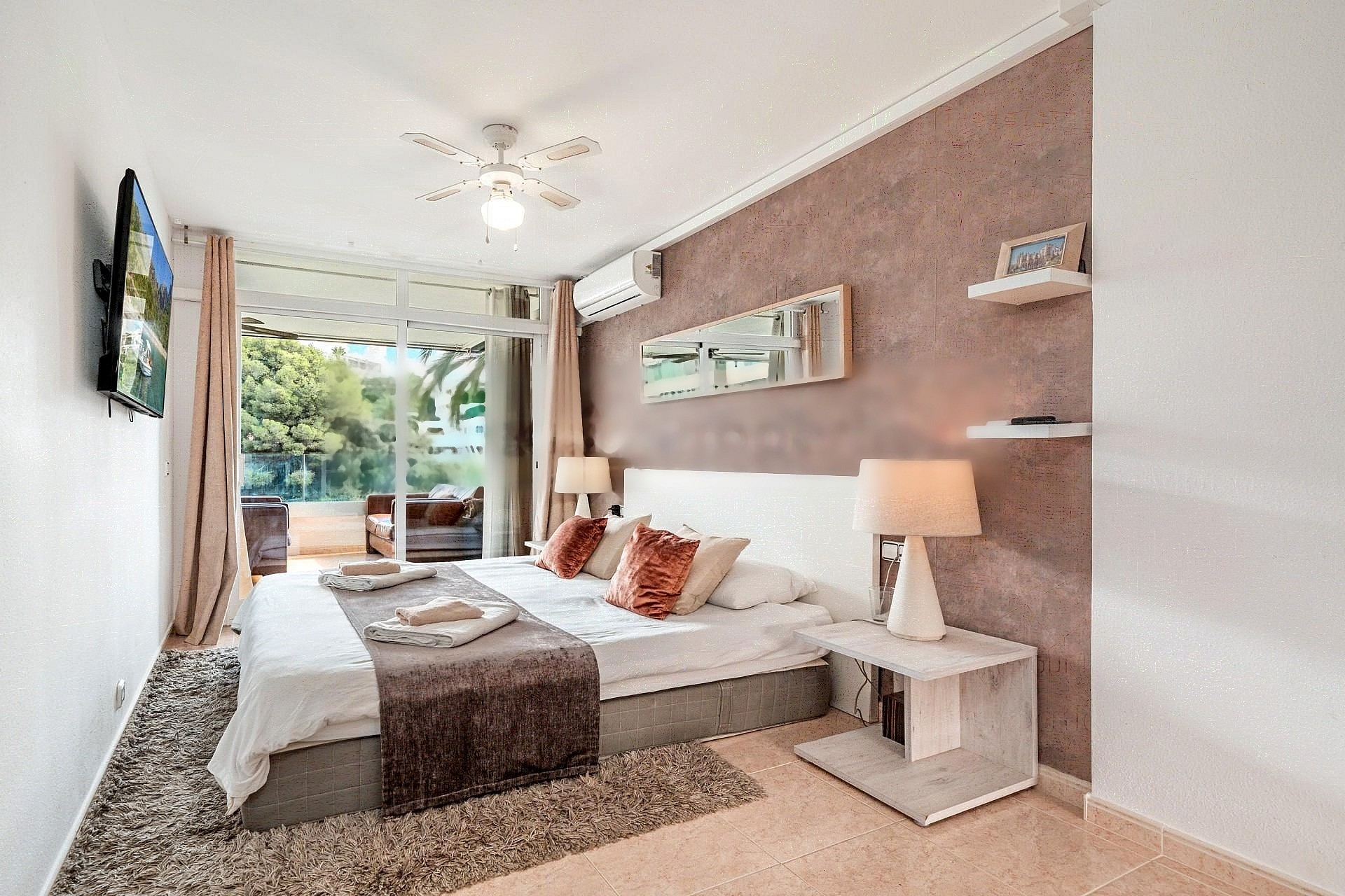 A modern bedroom featuring a large bed with neutral linens, a textured terracotta feature wall, and glass sliding doors leading to a private terrace.