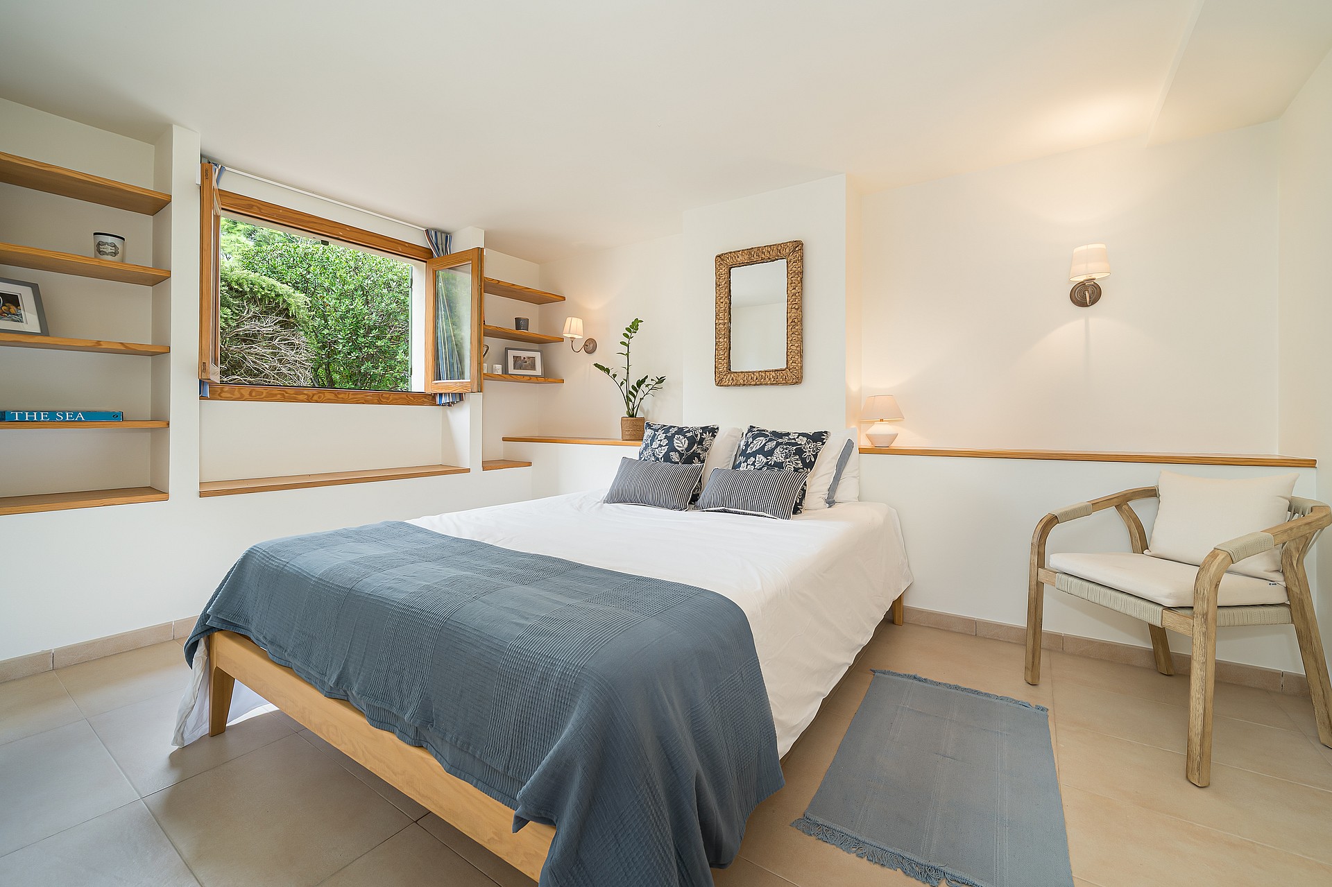 Bright bedroom featuring a wooden bed frame, custom oak shelves, and a window overlooking a lush garden wall.