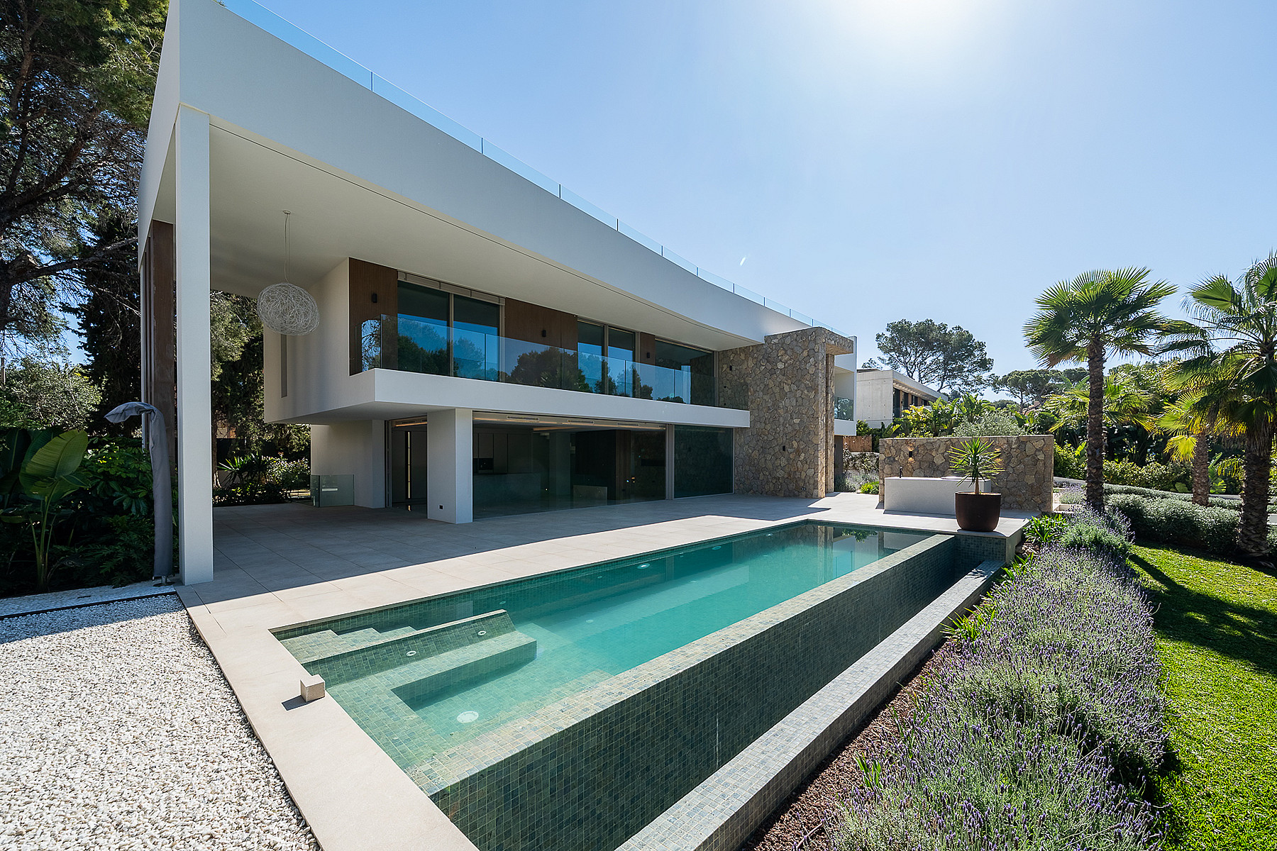 Contemporary white villa in Santa Ponsa with a long rectangular swimming pool, stone accent wall, and landscaped garden.