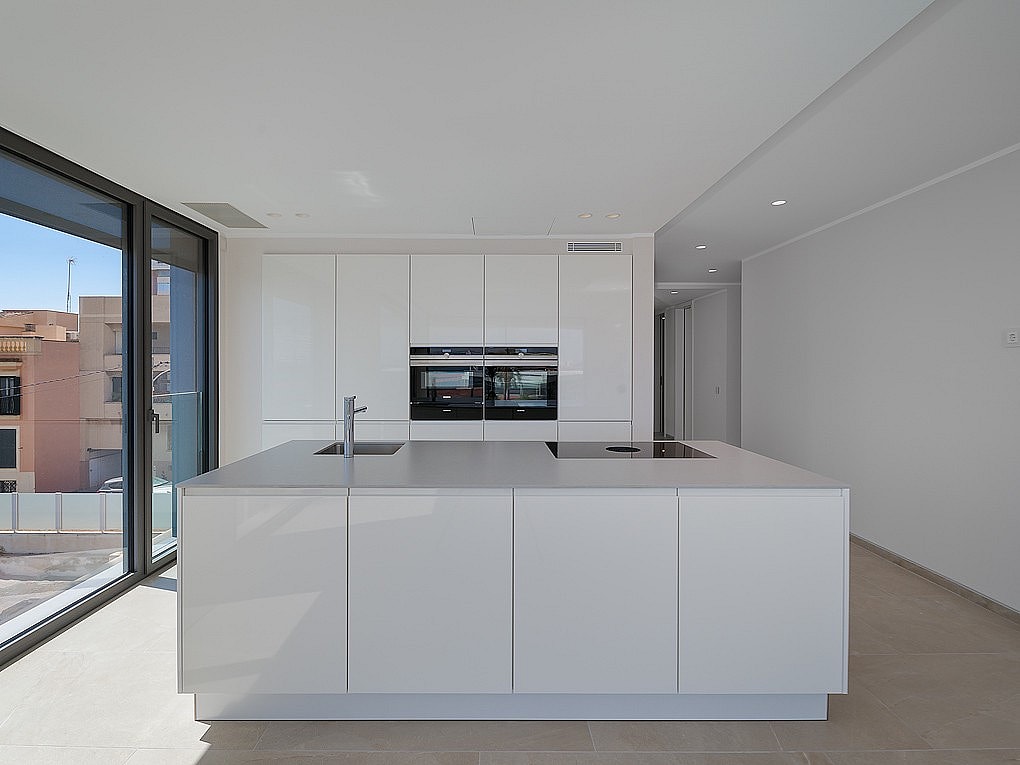 Integrated white kitchen and living area with large sliding glass doors opening to terrace and sea view