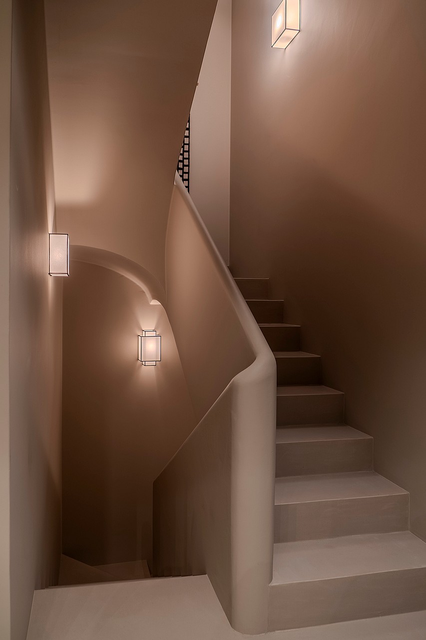 A minimalist internal staircase featuring curved plaster handrails and integrated warm wall sconces in soft sand tones.