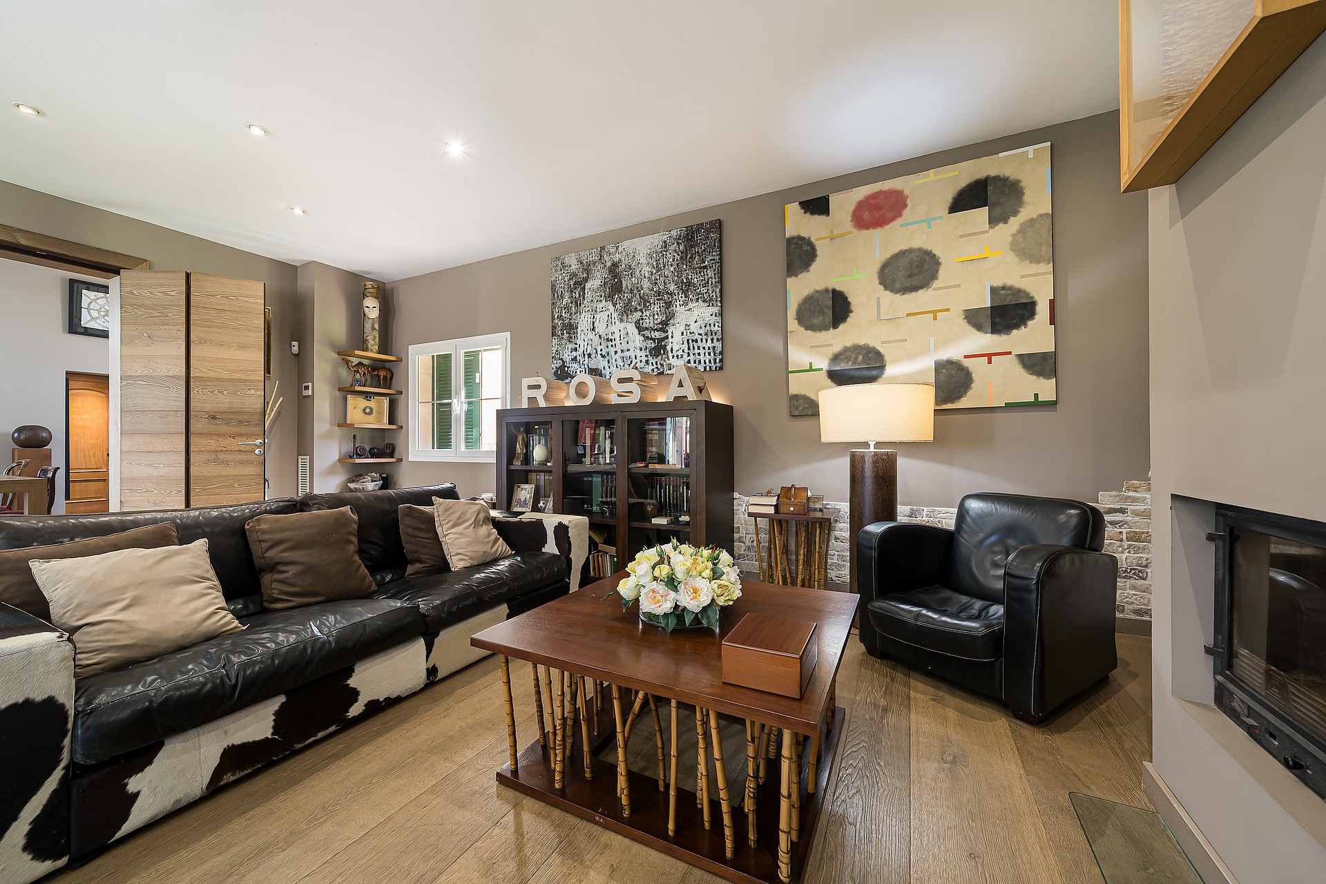 Interior view of a living room with dark leather sofas, a wooden coffee table, large abstract art, and a recessed fireplace.