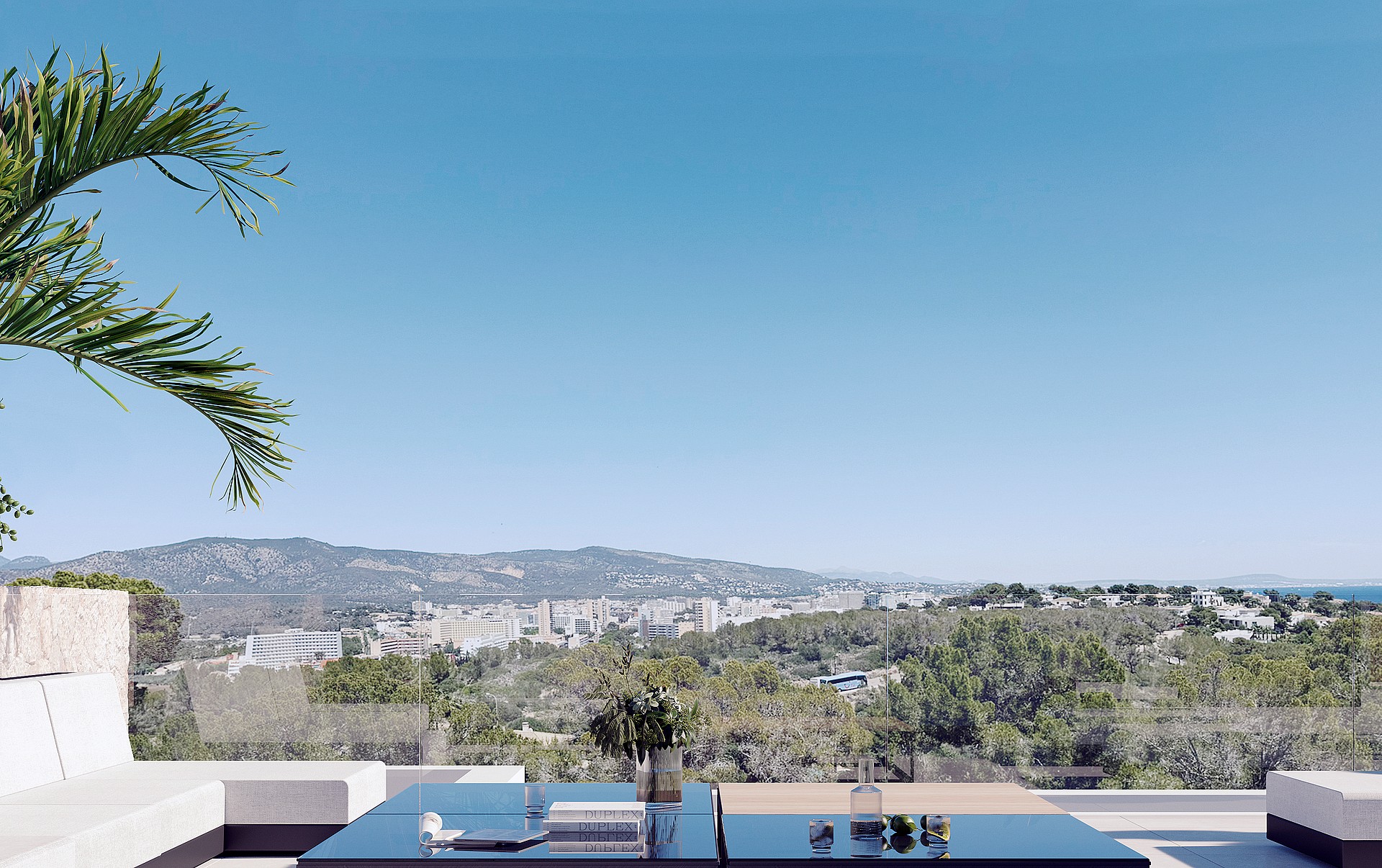 An outdoor terrace with white minimalist sofa and glass-topped table overlooking a valley, cityscape, and mountain range.