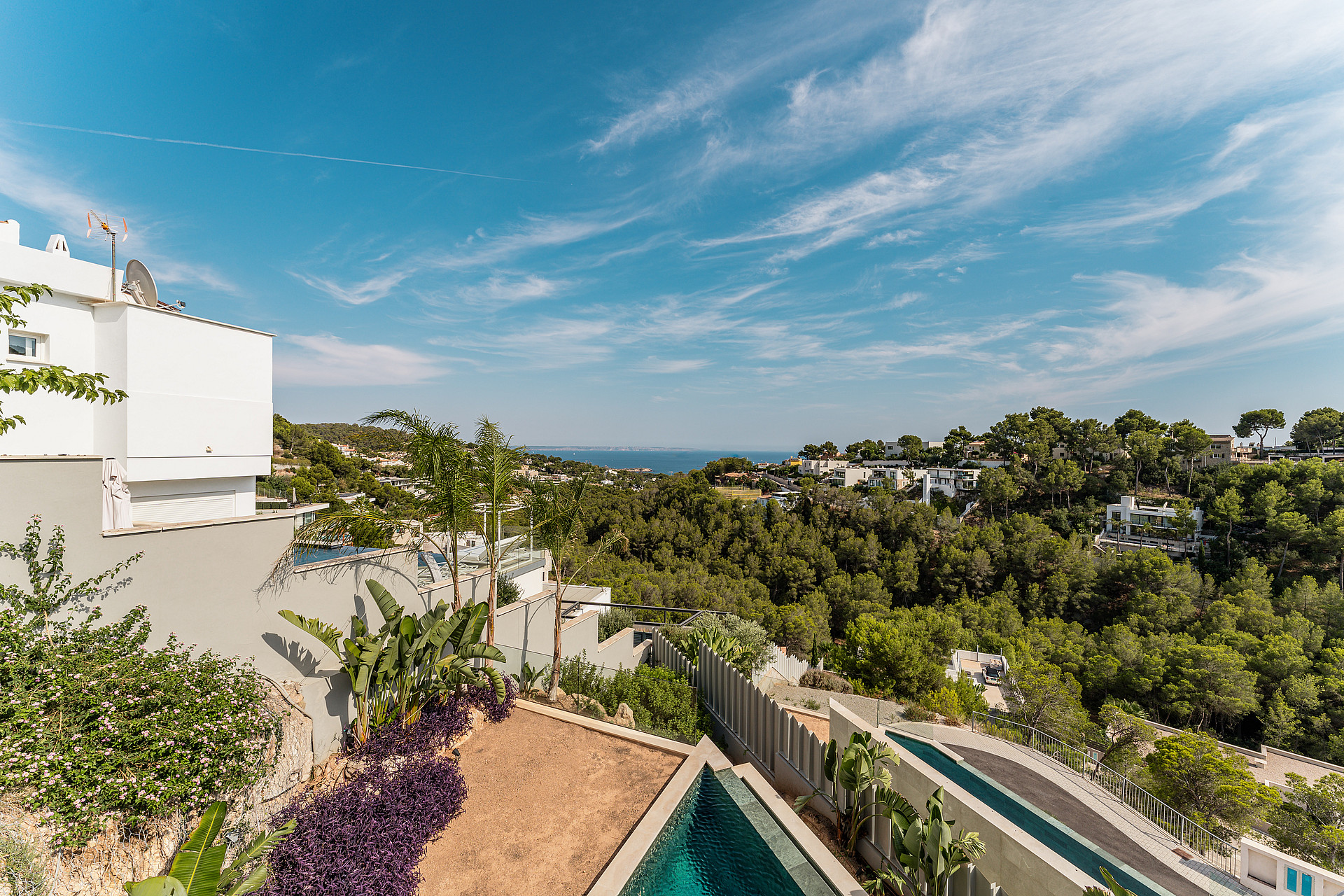 High angle shot of a minimalist white villa exterior with a swimming pool and landscaped garden overlooking the Mediterranean coastline.