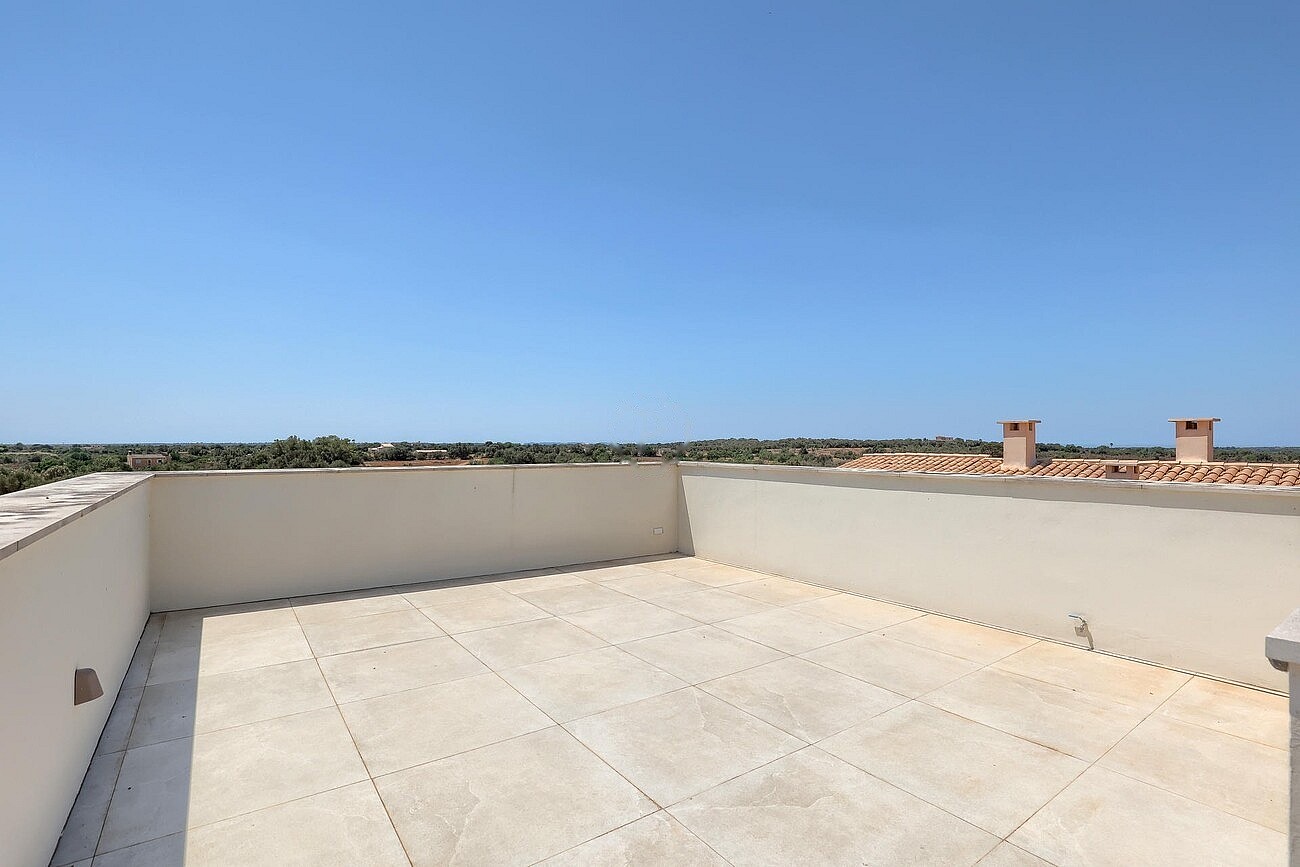 Empty rooftop terrace with pale stone tiling and low plastered walls under a clear blue sky, overlooking distant countryside.