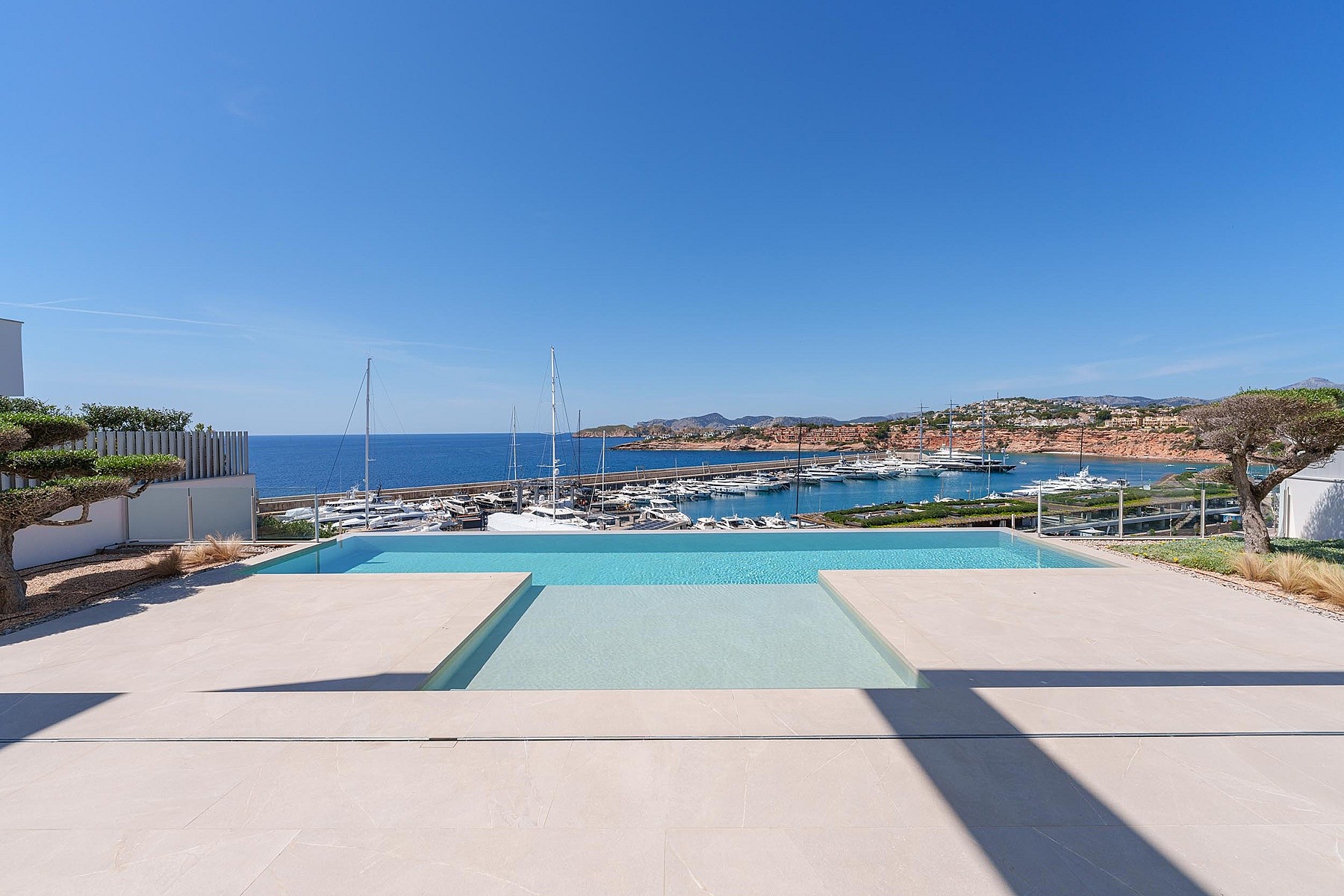 A rectangular swimming pool with a shallow step entry, overlooking a marina and the open Mediterranean sea under a clear sky.
