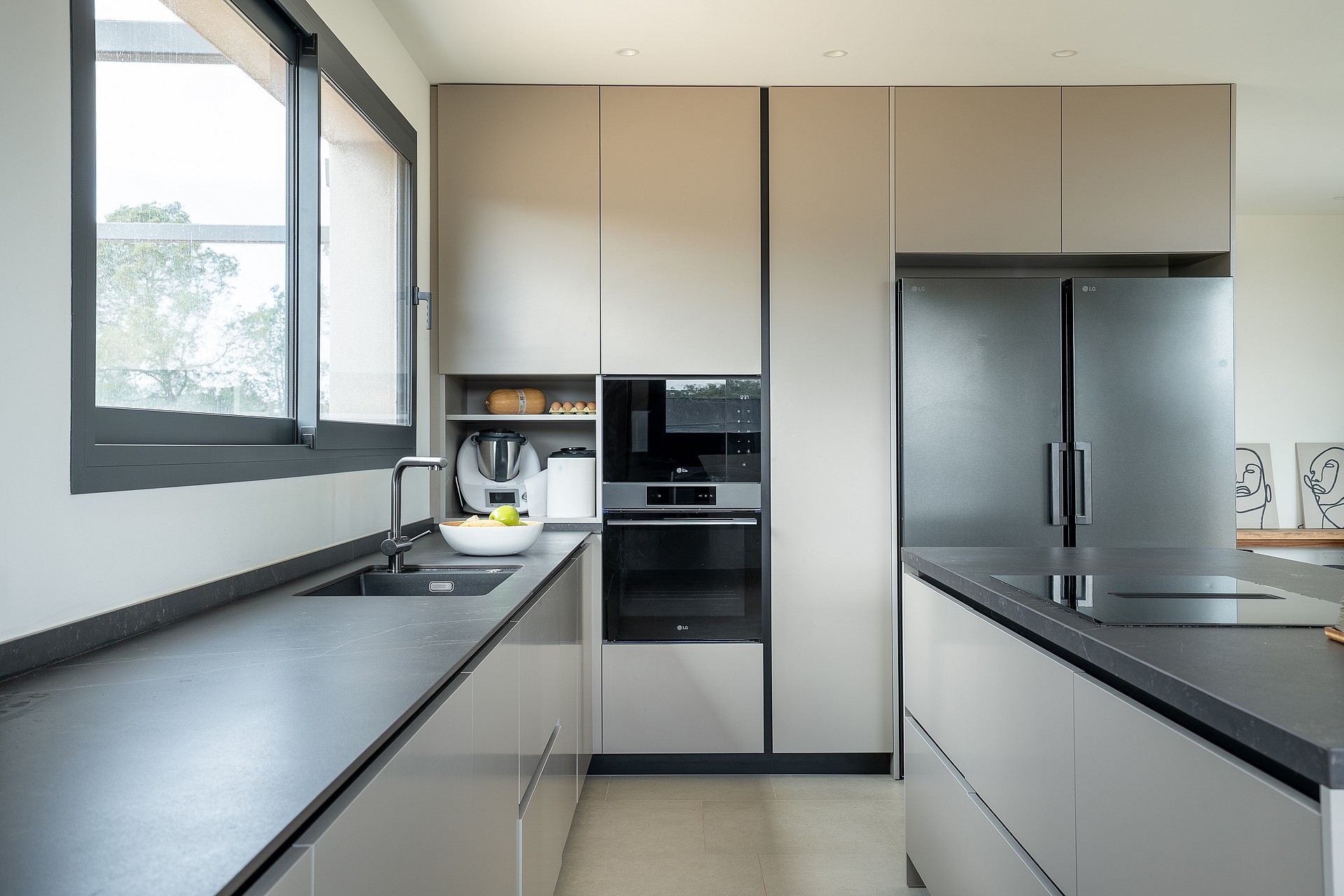 Modern kitchen featuring matte grey cabinetry, dark stone countertops, integrated stainless steel appliances, and large window.