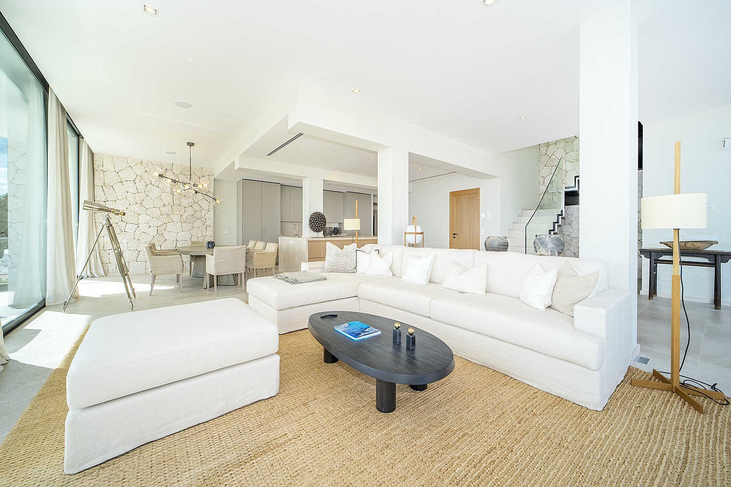 Bright open-plan living room in Illetas with white sectional sofa, oval coffee table, and a large textured jute rug.