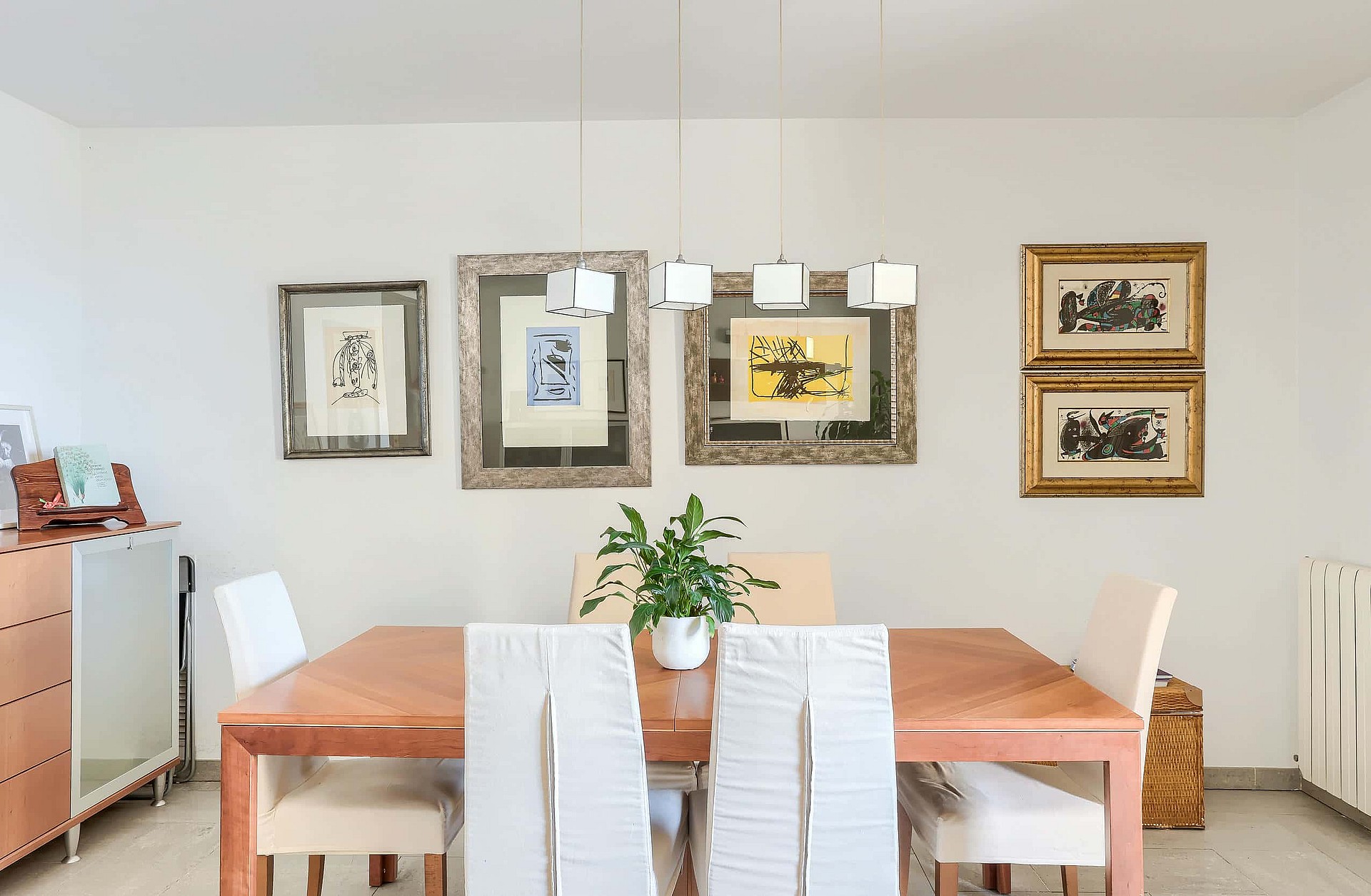 Dining area featuring a rectangular wooden table, four white upholstered chairs, and a gallery wall with framed prints.