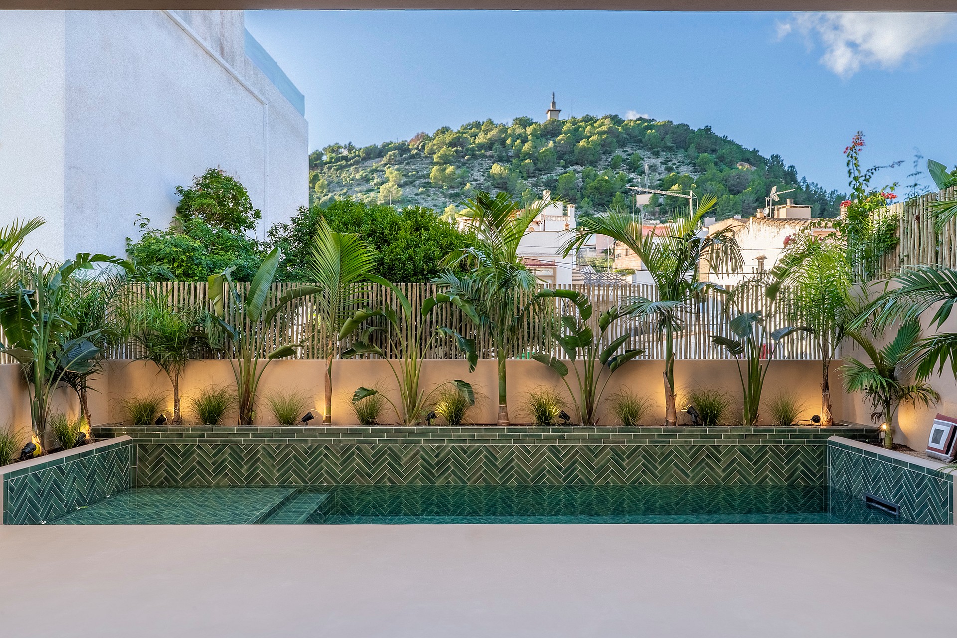 A rectangular pool with green chevron tiling and tropical plants, set against a backdrop of the Na Burguesa hills.