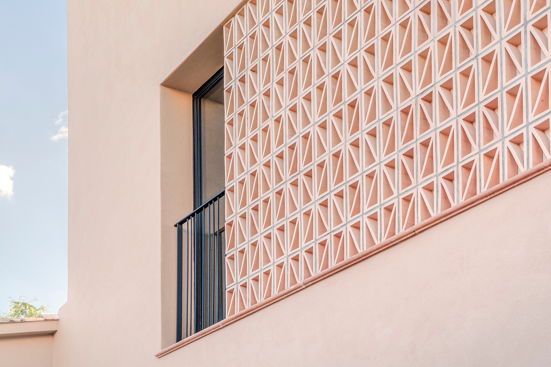 Close-up of a pink plastered townhouse exterior featuring a geometric terracotta breeze block screen and black metal railing.