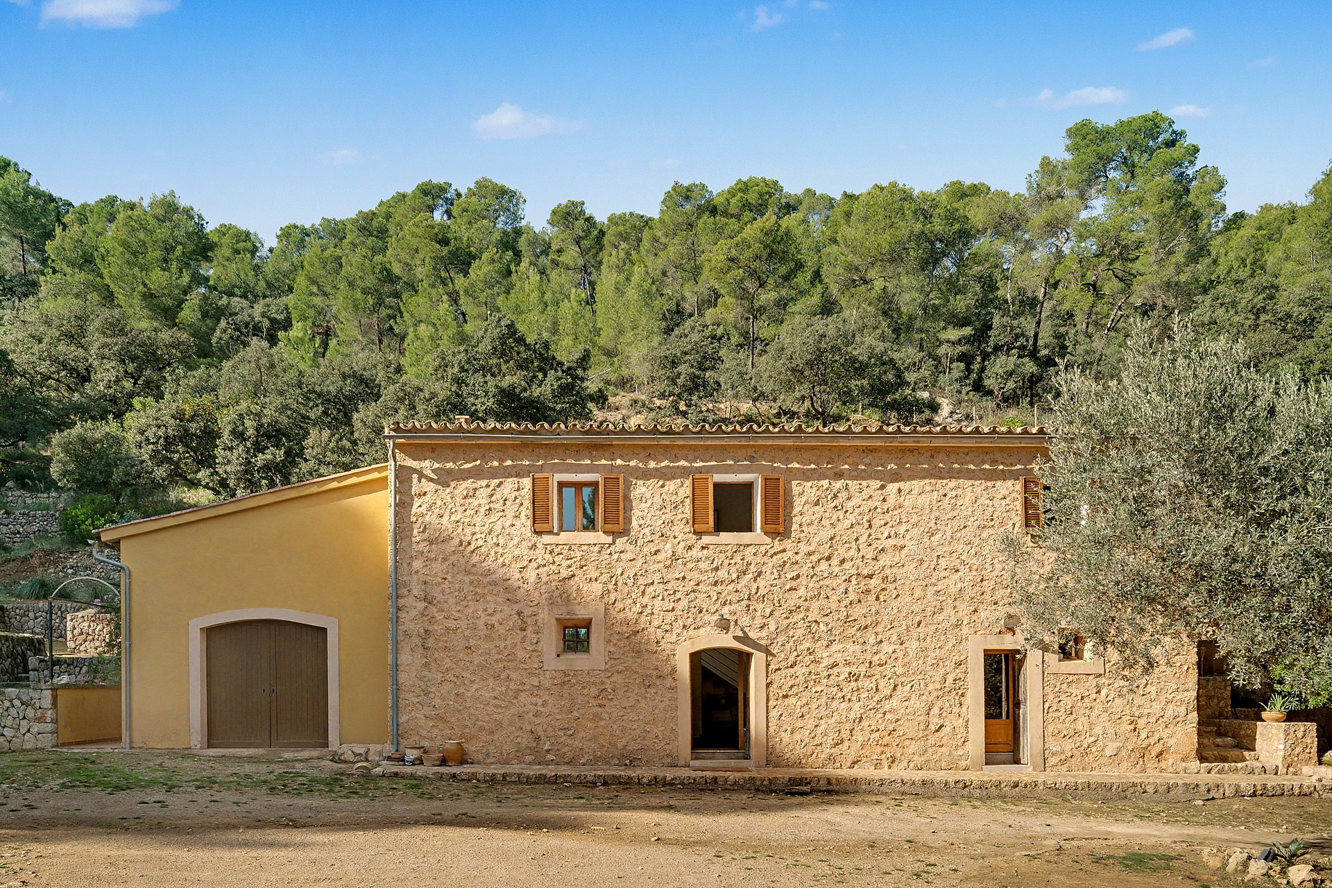 Two-storey stone finca façade with wooden shutters and dry-stone walls