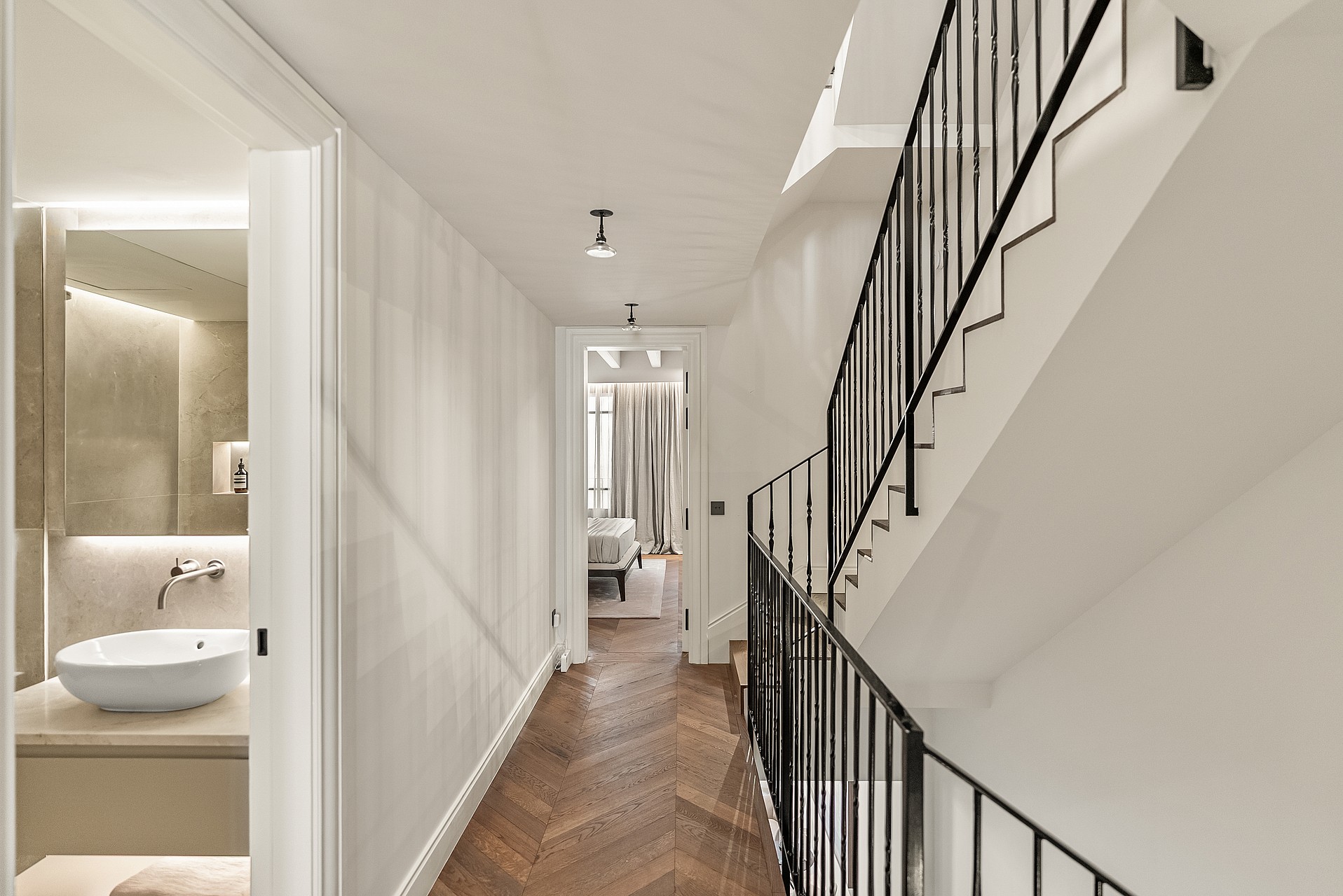 Interior hallway featuring herringbone wood floors, black metal staircase railings, and a view into a bedroom.